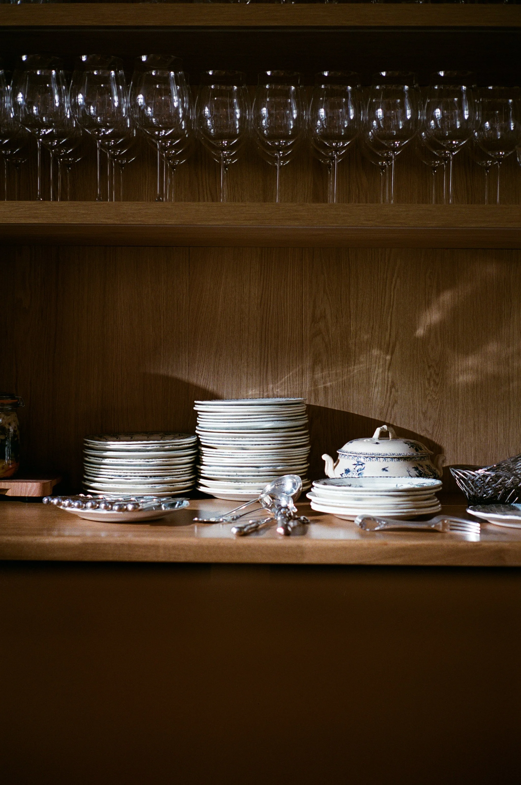 Vaisselle en porcelaine, verres à vin, couverts en argent, et pot à thé dans une étagère en bois