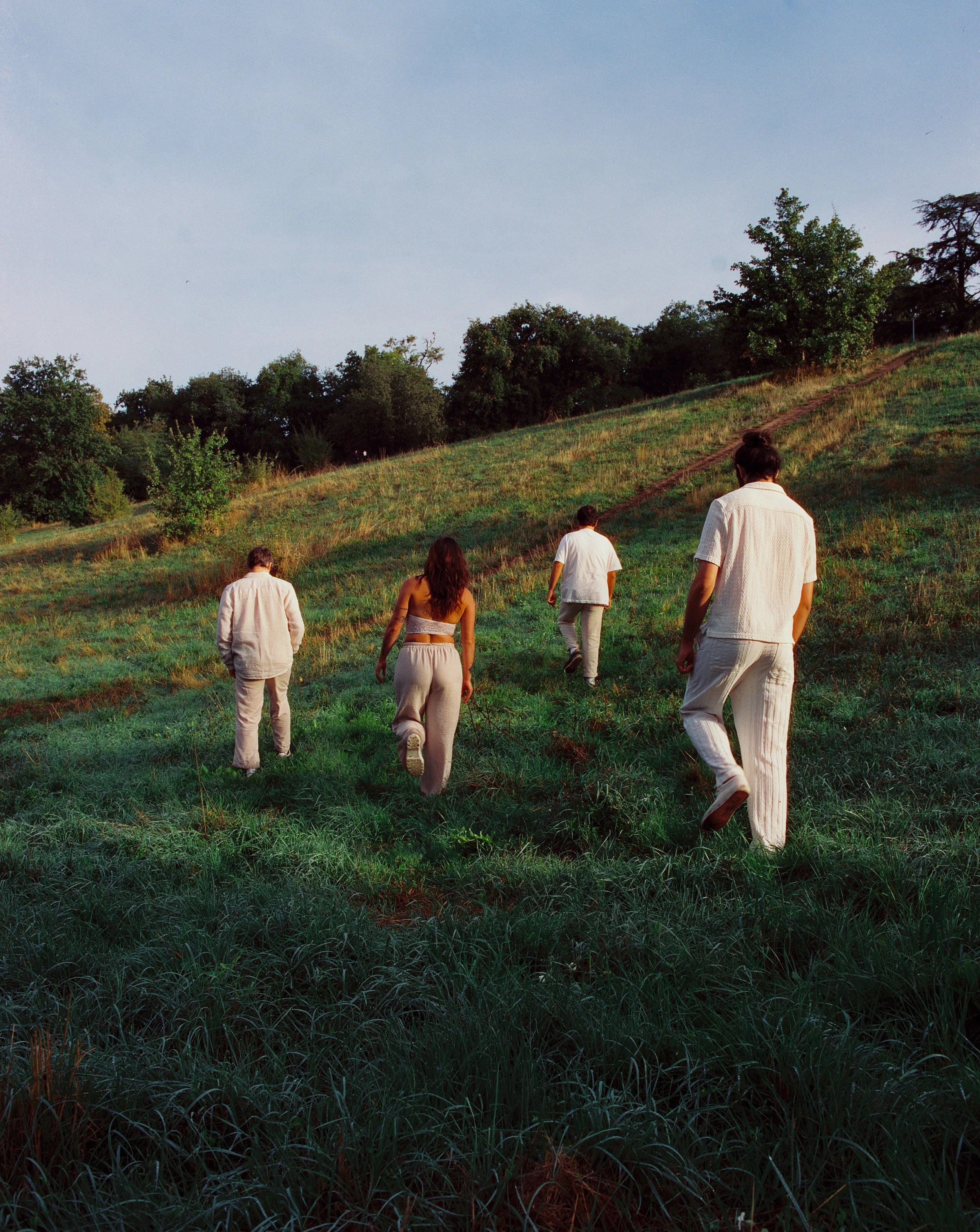 Cinq personnes marchant en montée sur une colline verdoyante, entourées d'arbres, sous un ciel clair au crépuscule.