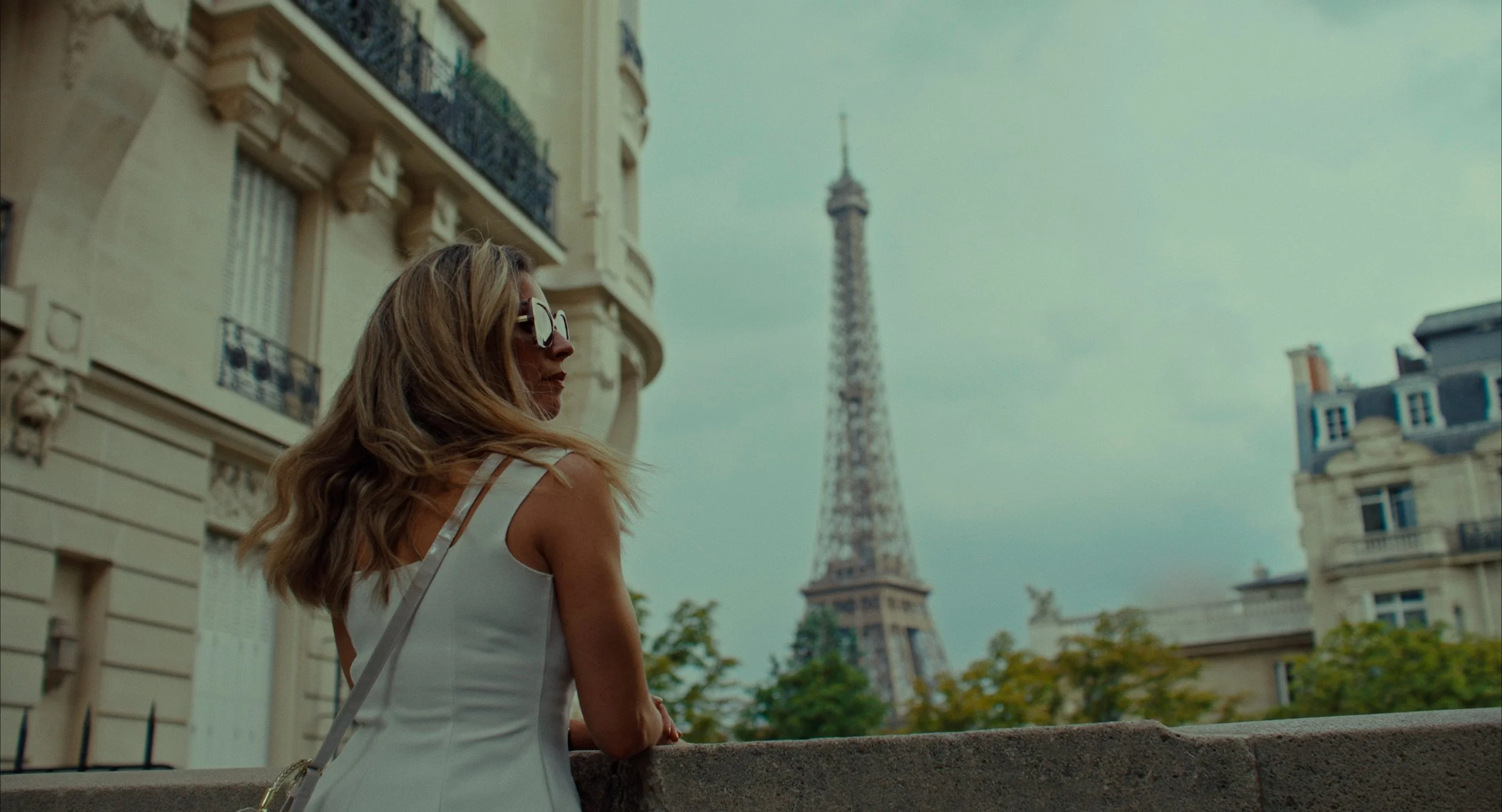 Une femme portant des lunettes de soleil et une robe blanche regarde vers la Tour Eiffel à Paris.