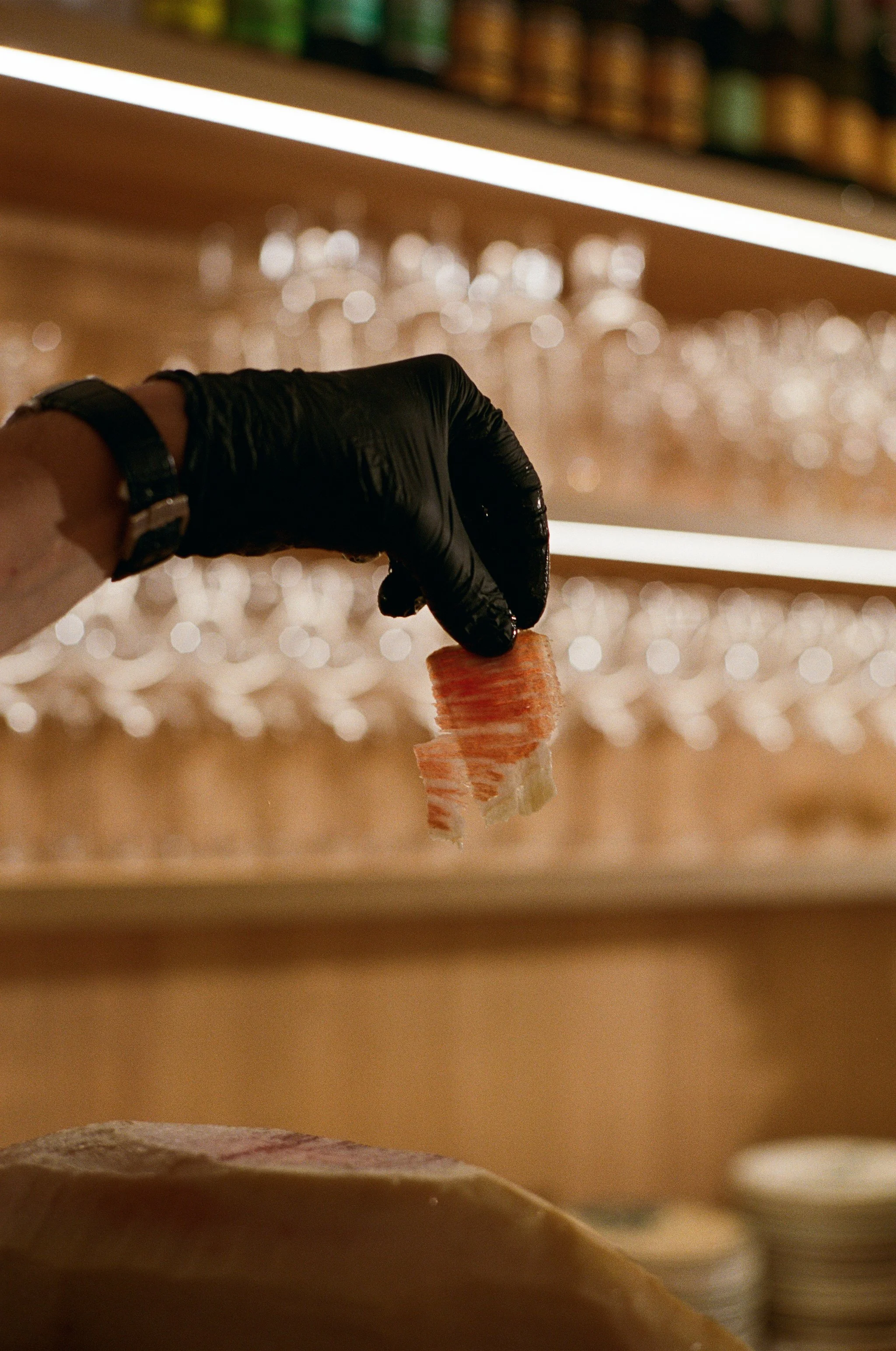 Une main portant un gant noir tient une tranche de crabes de imitation ou de saumon dans un restaurant ou un comptoir de sushi.