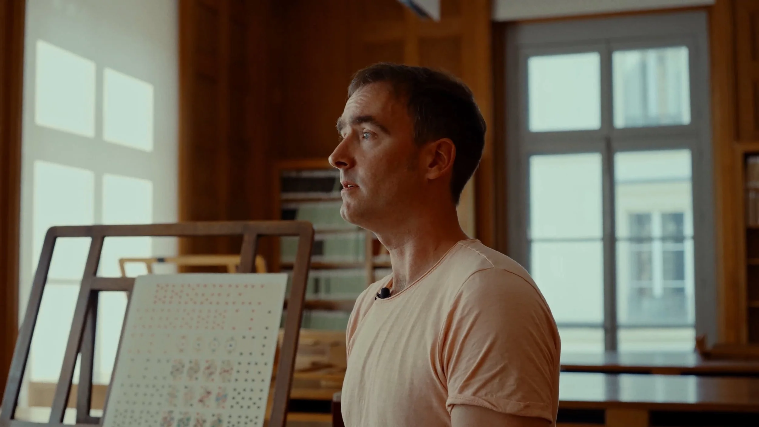 Jeune homme de profil dans une bibliothèque en bois avec grandes fenêtres