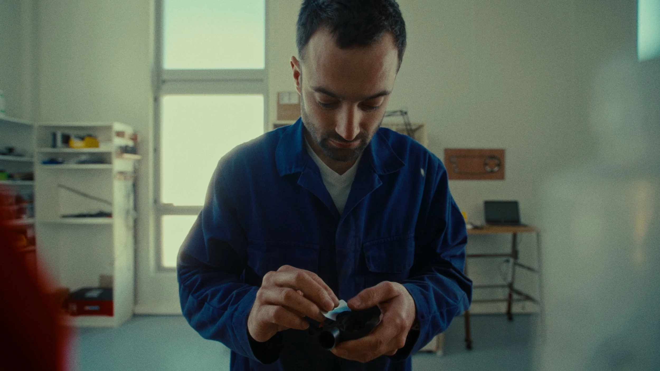 Un homme en blouse bleue examinant un objet dans ses mains dans une pièce lumineuse.