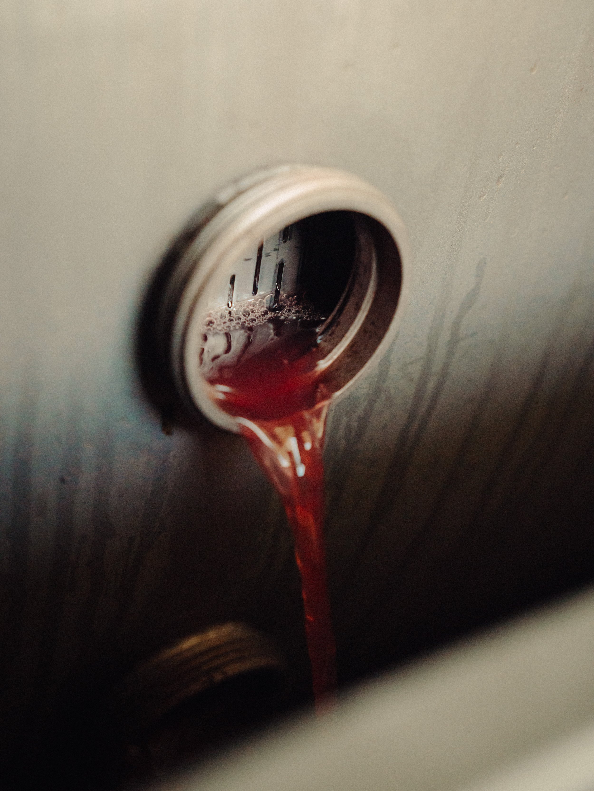 Une photo montrant du vin rouge coulant d'une cuve ou d'un tuyau dans une cave ou un bar.