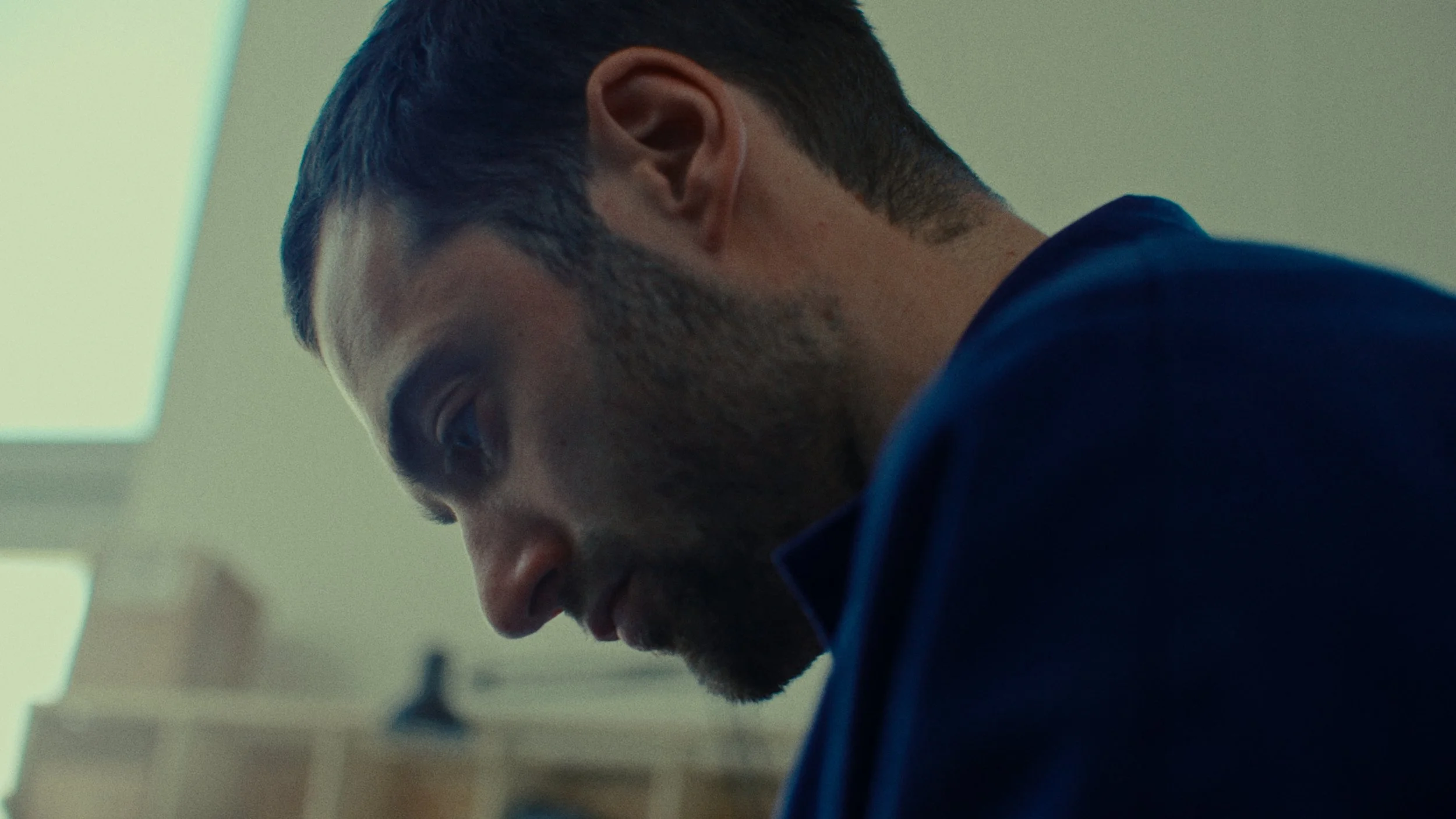 Un homme avec une barbe courte, portant un vêtement bleu, vu en profil dans un environnement intérieur