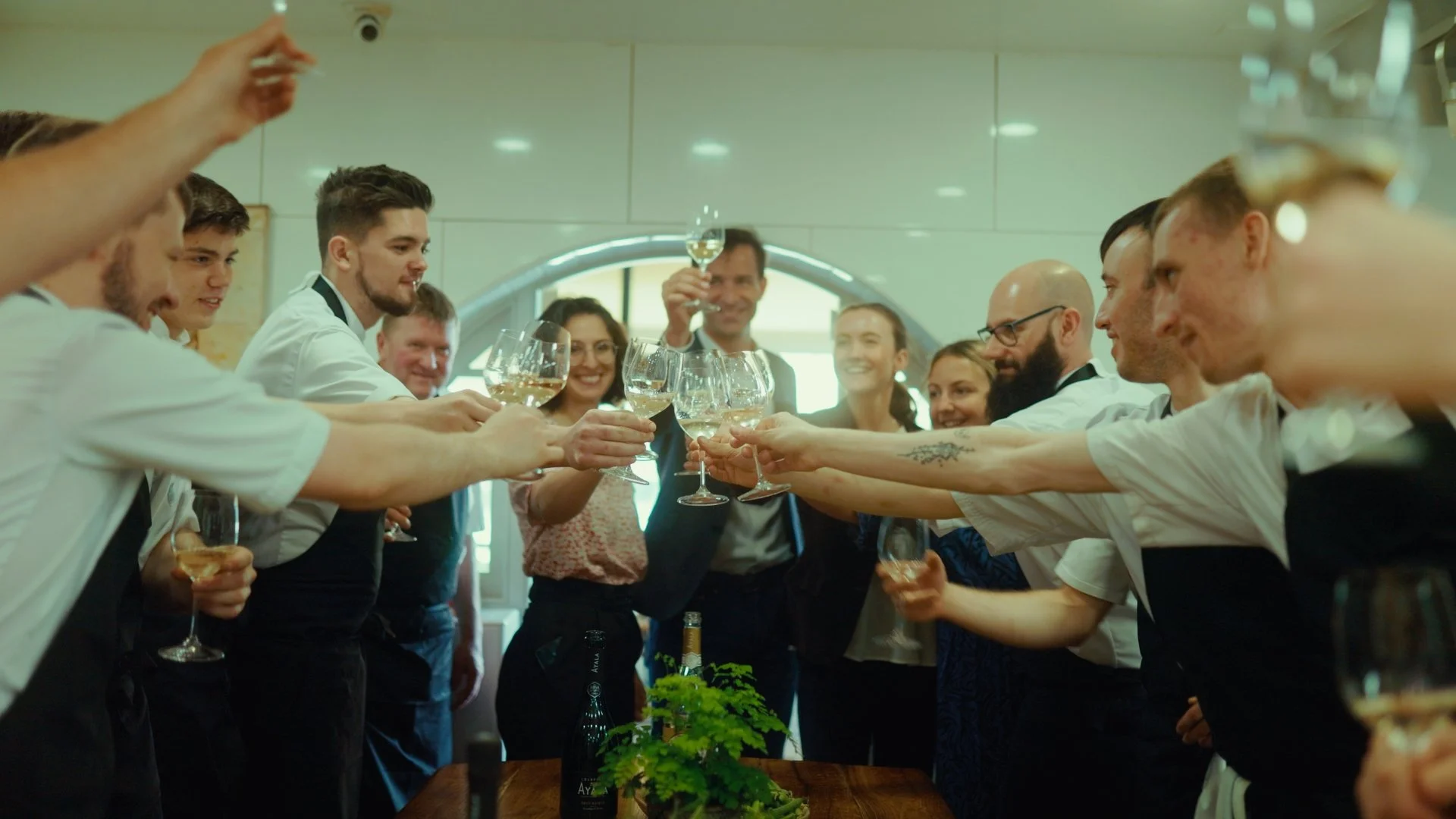 Groupe de personnes en tenue de cuisine faisant un toast avec des verres de vin blanc dans une cuisine moderne