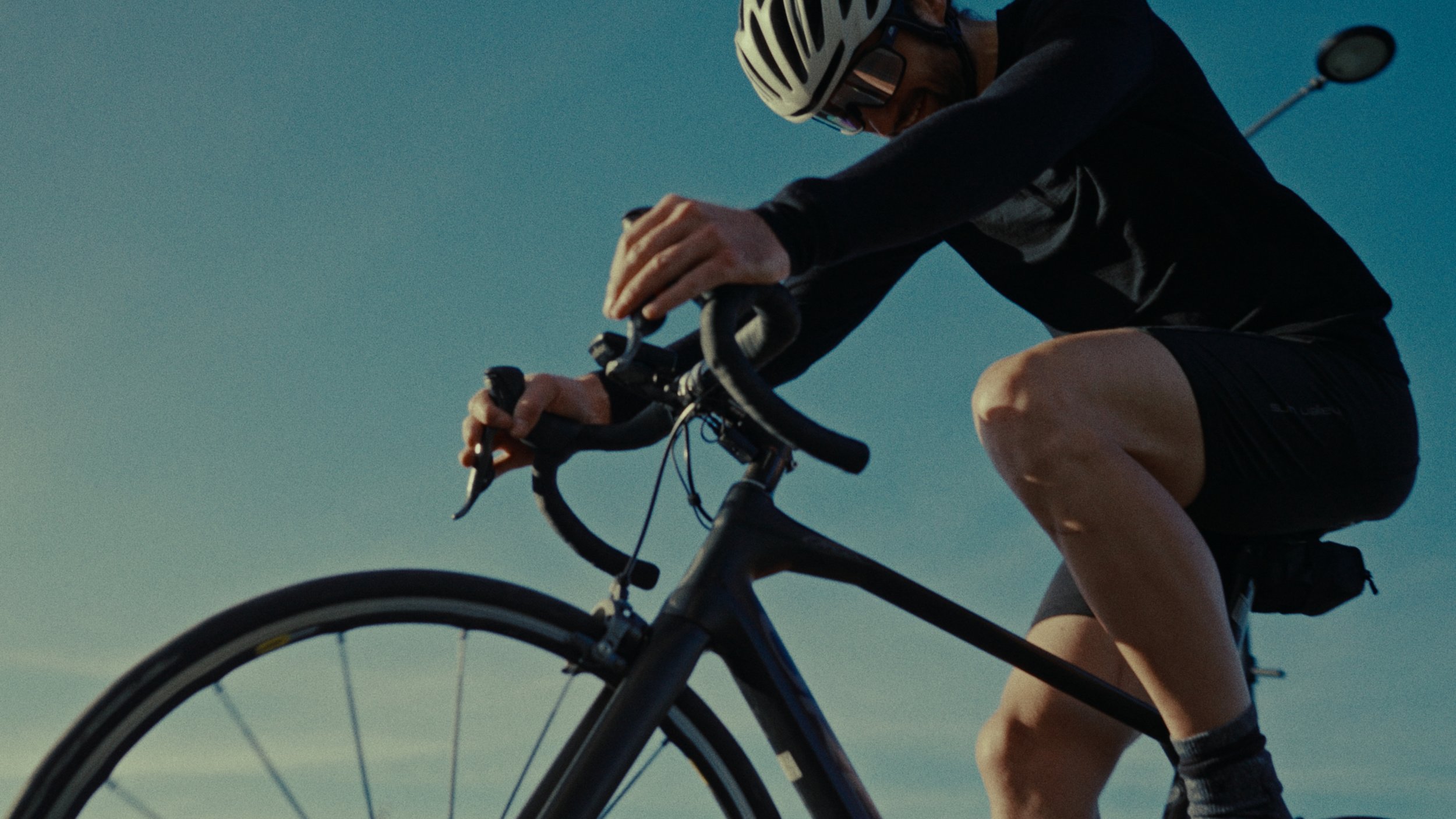 Un cycliste portant un casque et des vêtements sportifs en train de faire du vélo sur un fond de ciel bleu.