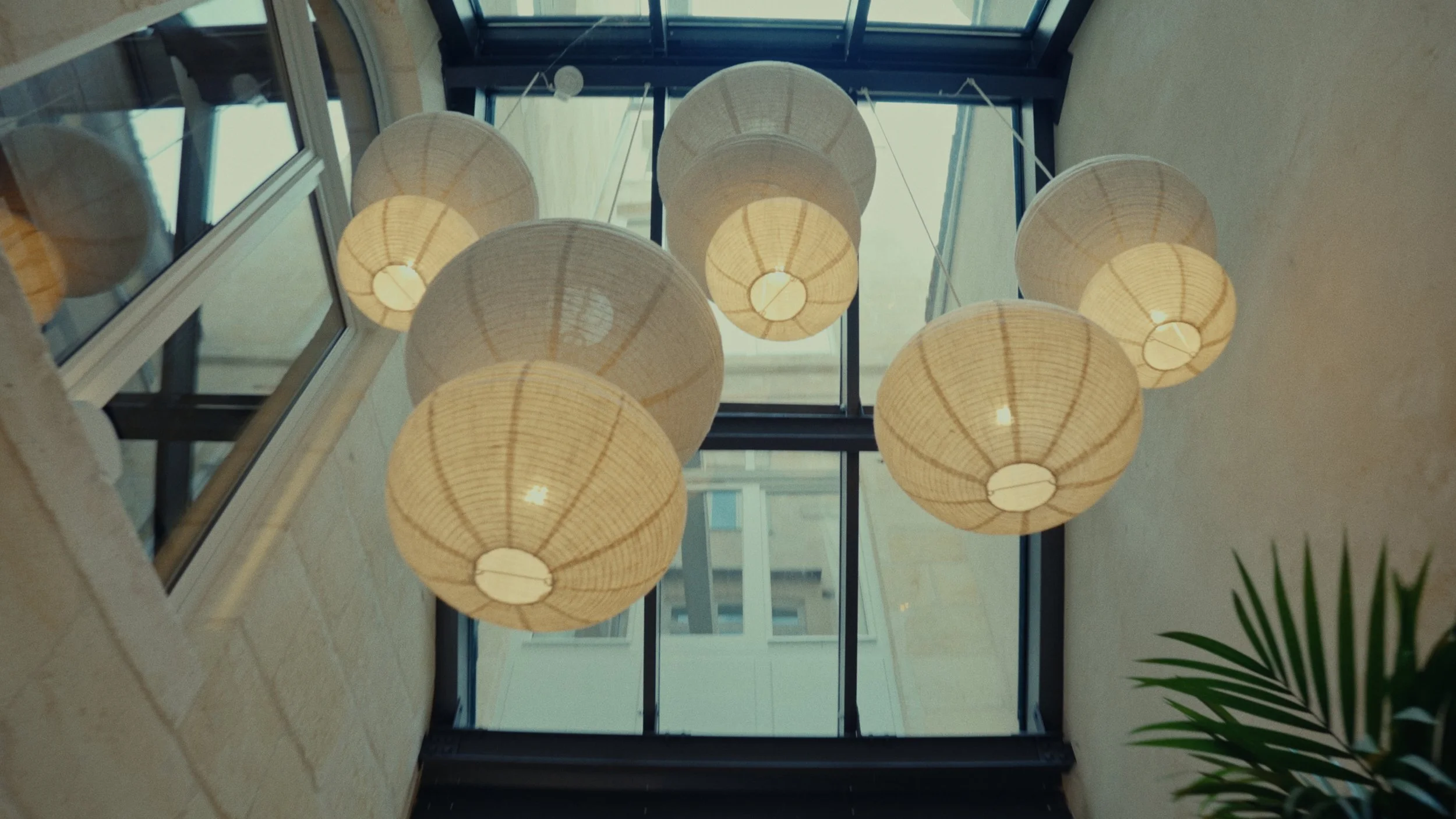 Plafond avec plusieurs lampes en forme de lanternes en papier suspendues dans un atrium avec un plafond en verre.