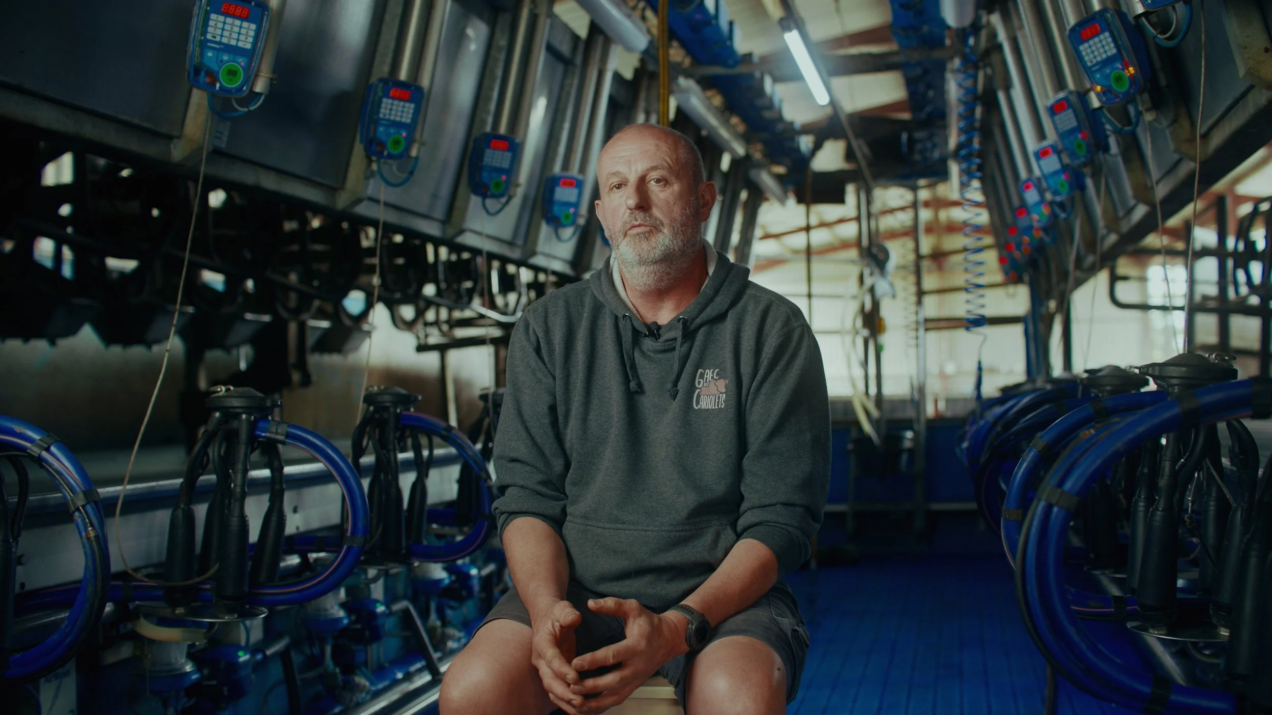 Un homme assis dans une salle remplie de machines et d'équipements, regardant sérieusement vers l'objectif.