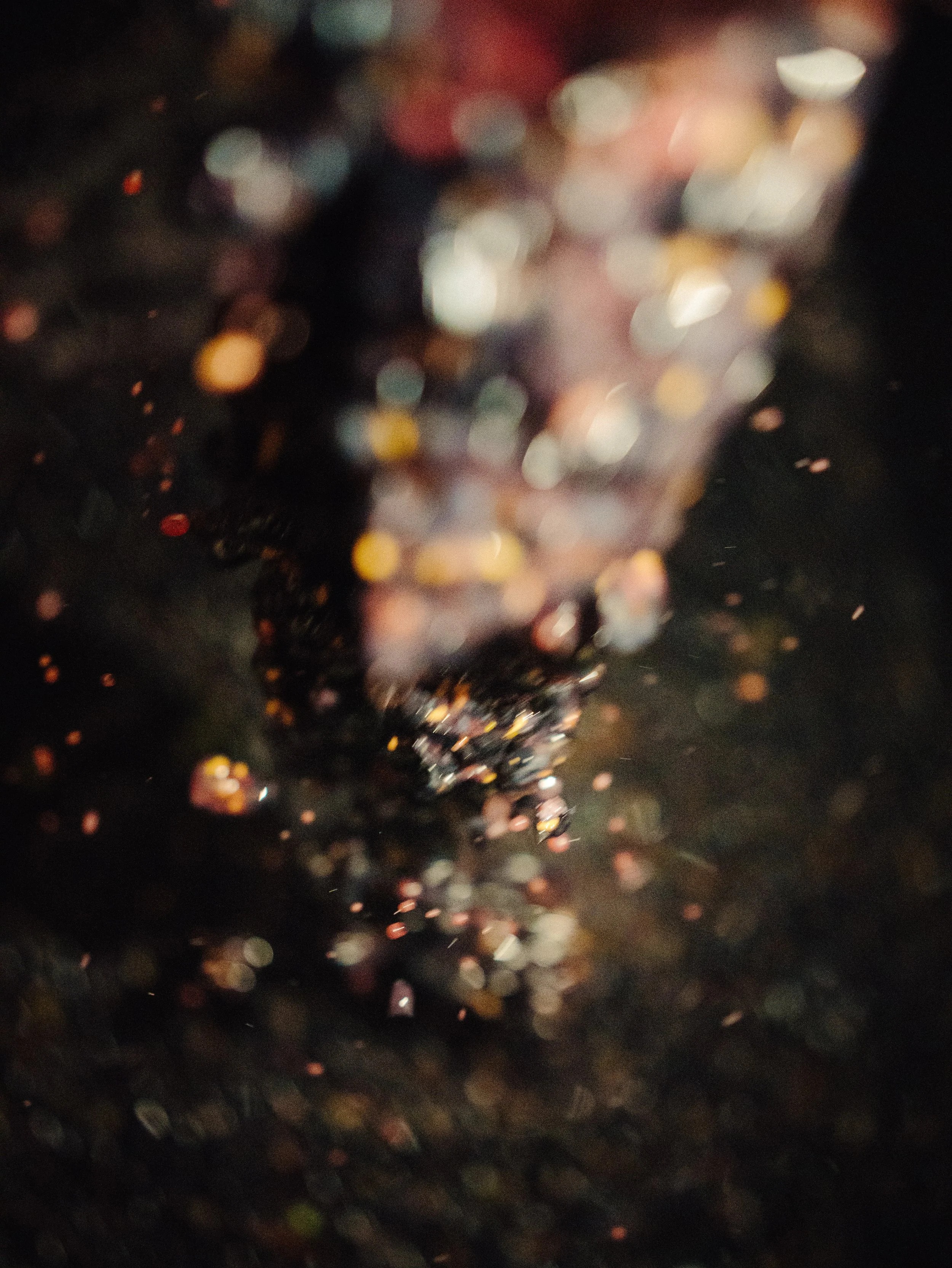 Gouttes d'eau tombant sur une surface sombre, créant des éclats de lumière flous et colorés.