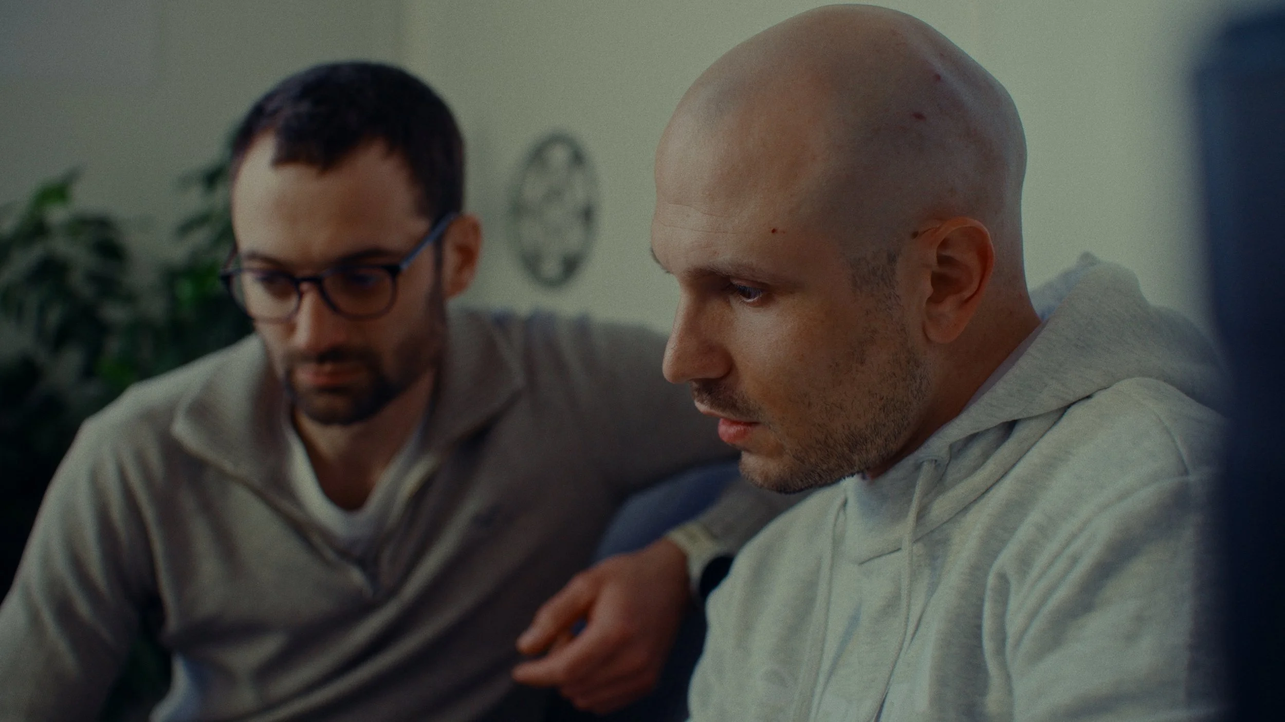 Deux hommes assis sur un canapé, l'un en train d'écouter sérieusement, l'autre avec une expression concentrée.
