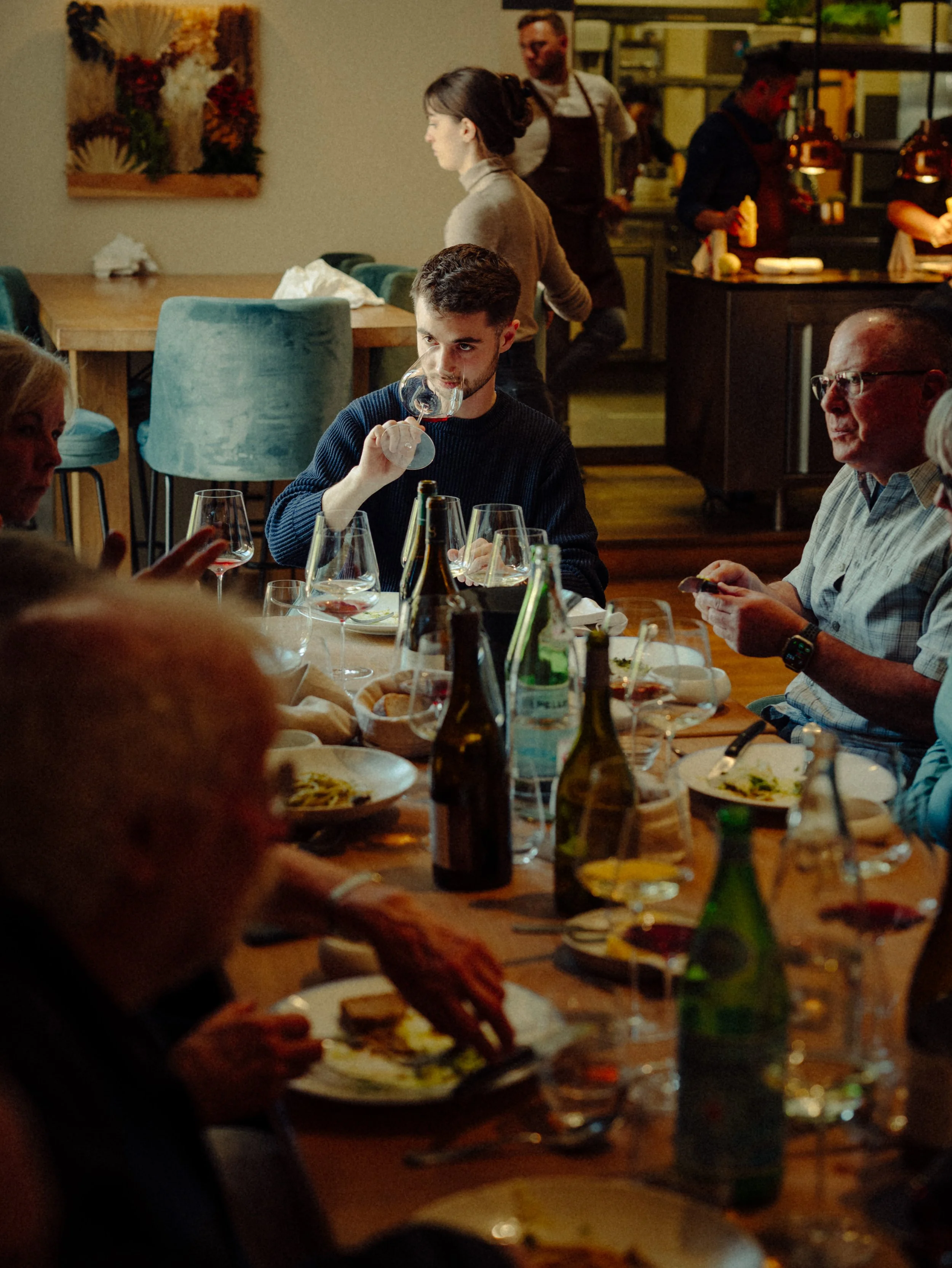 Groupe de personnes autour d'une table en dîner, certains dégustant du vin, dans un restaurant.