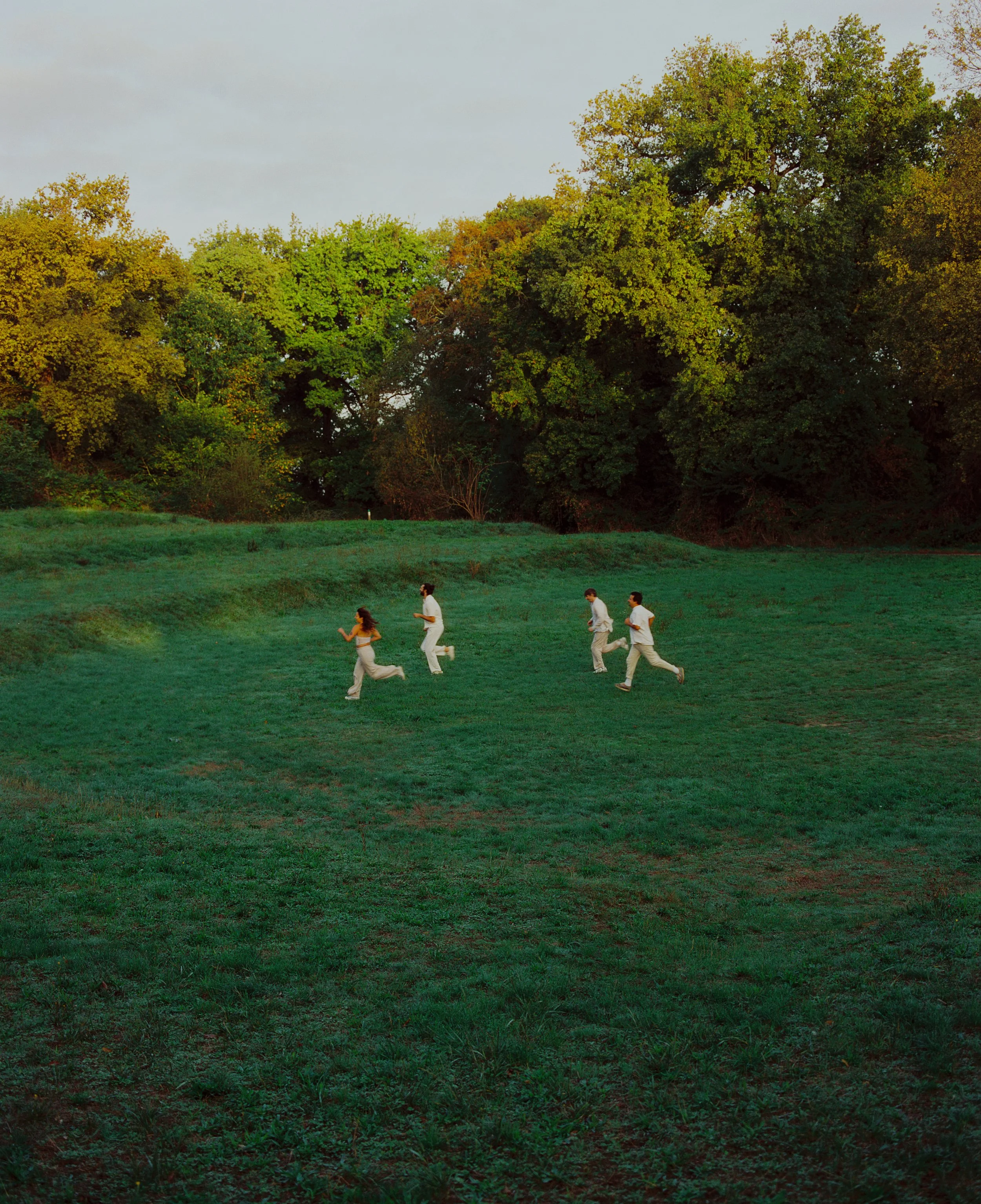 Groupe de quatre personnes courant dans un parc vert avec des grands arbres en arrière-plan.