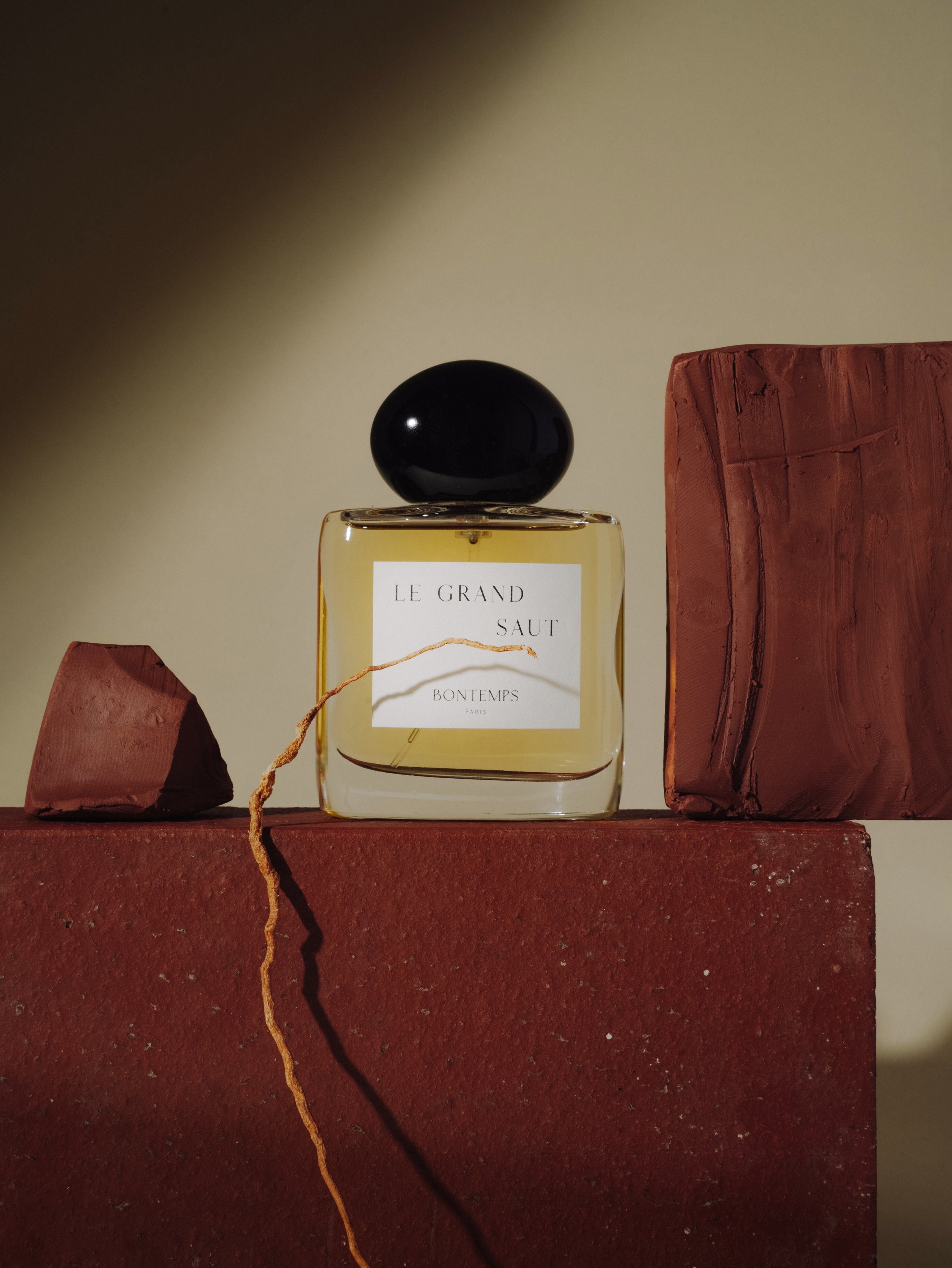 Une bouteille de parfum sur une surface en briques rouges, avec des blocs en brique derrière, sous un éclairage chaud.