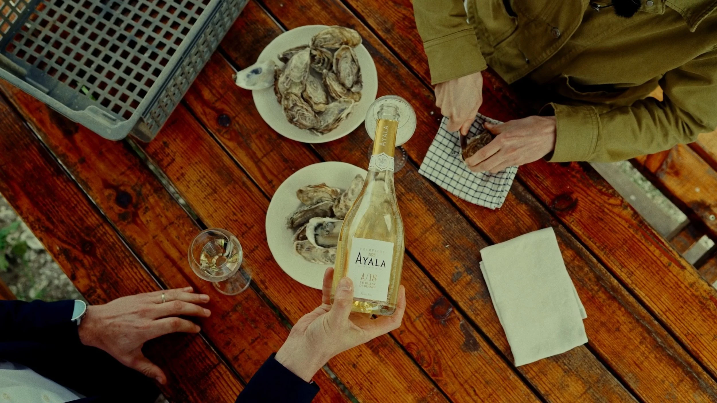 Personnes dégustant des huîtres à une table en bois avec une bouteille de champagne Ayala.