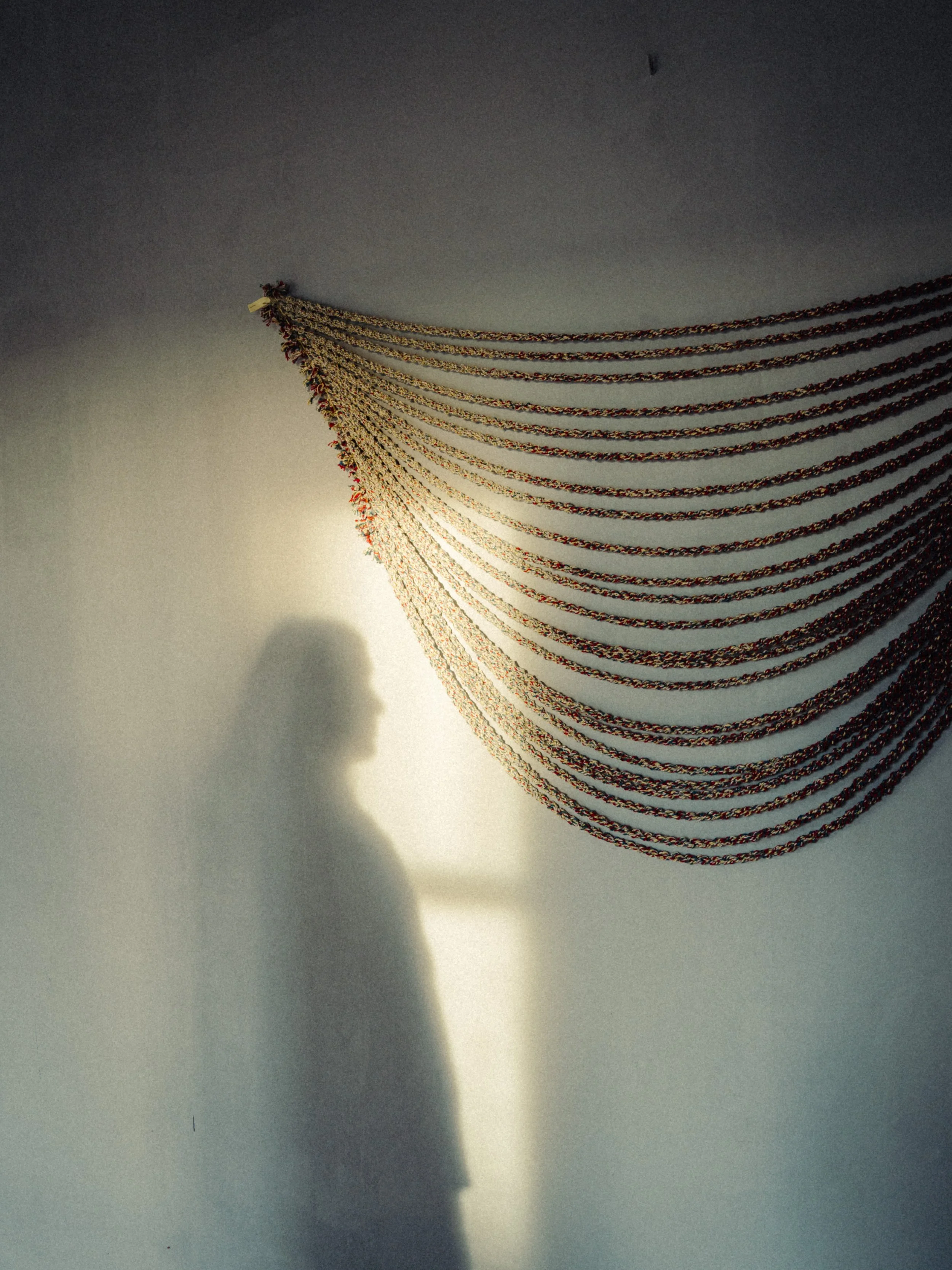 Silhouette d'une personne de profil, projetée sur un mur blanc, avec un décor de chaînes suspendues en forme de vague au plafond.