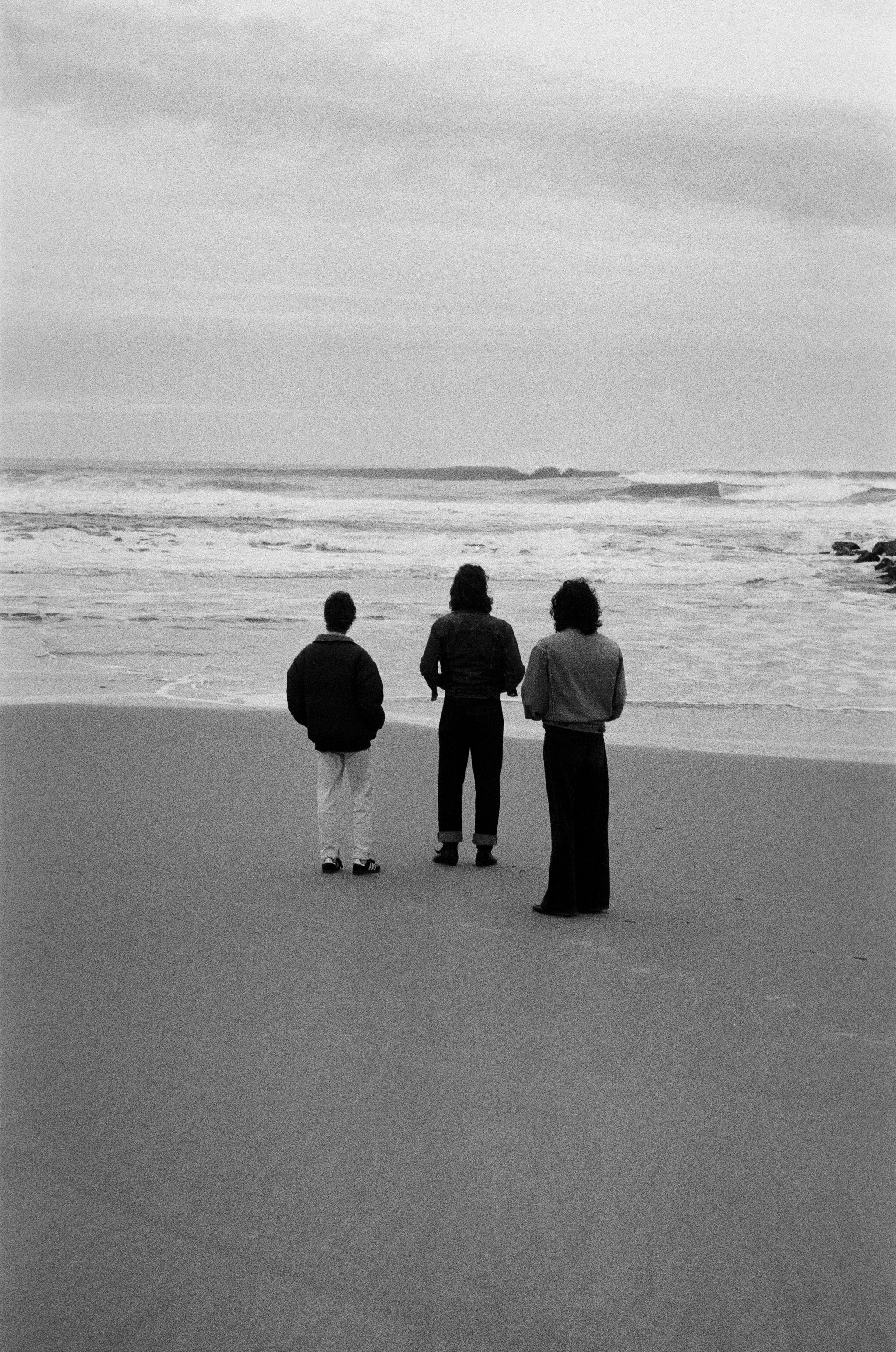 Trois personnes regardant la mer sur une plage, vue de dos, en noir et blanc.