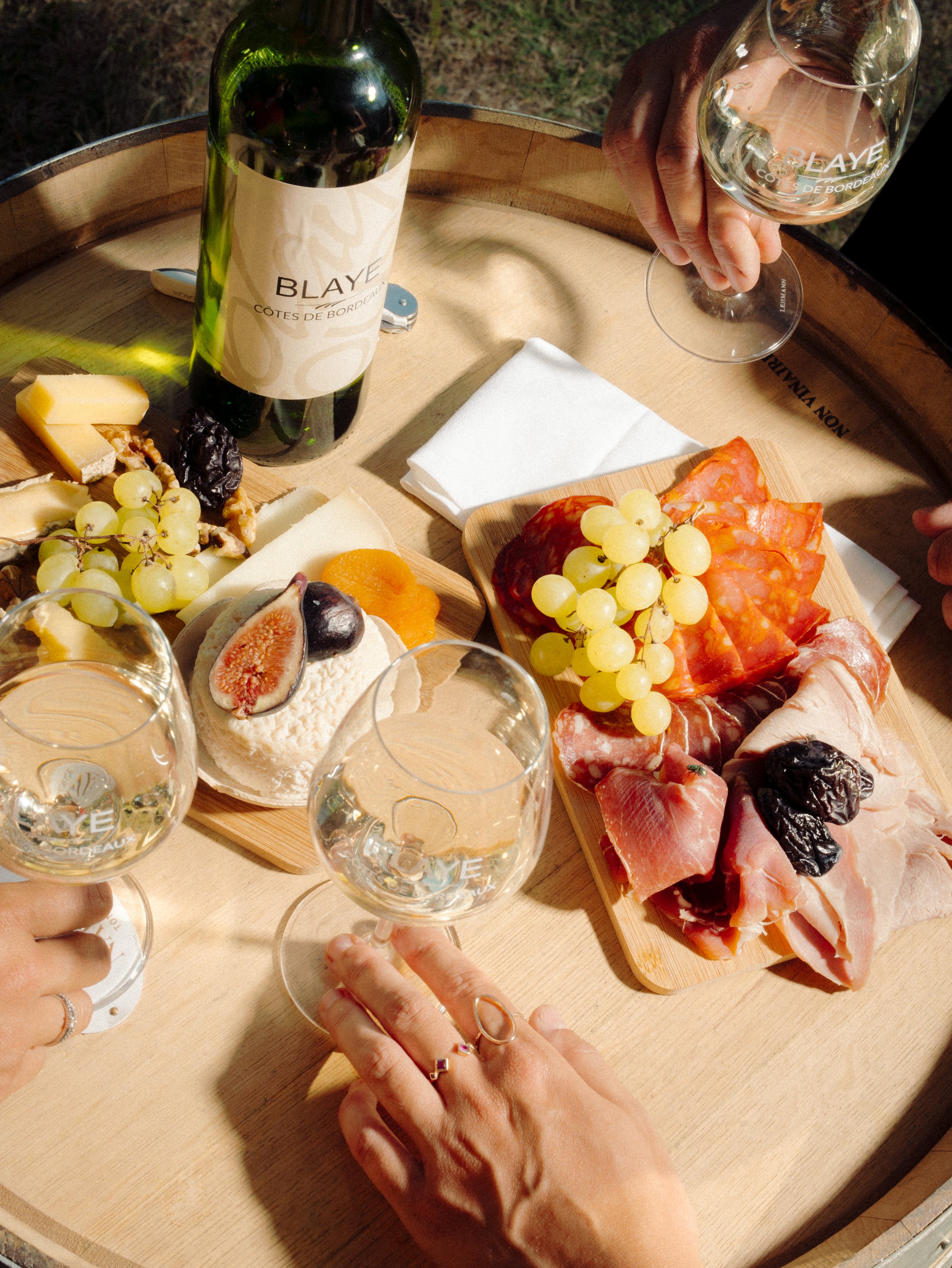 Plateau de fromages, charcuterie, raisins, figues, et fromage avec des verres de vin blanc.