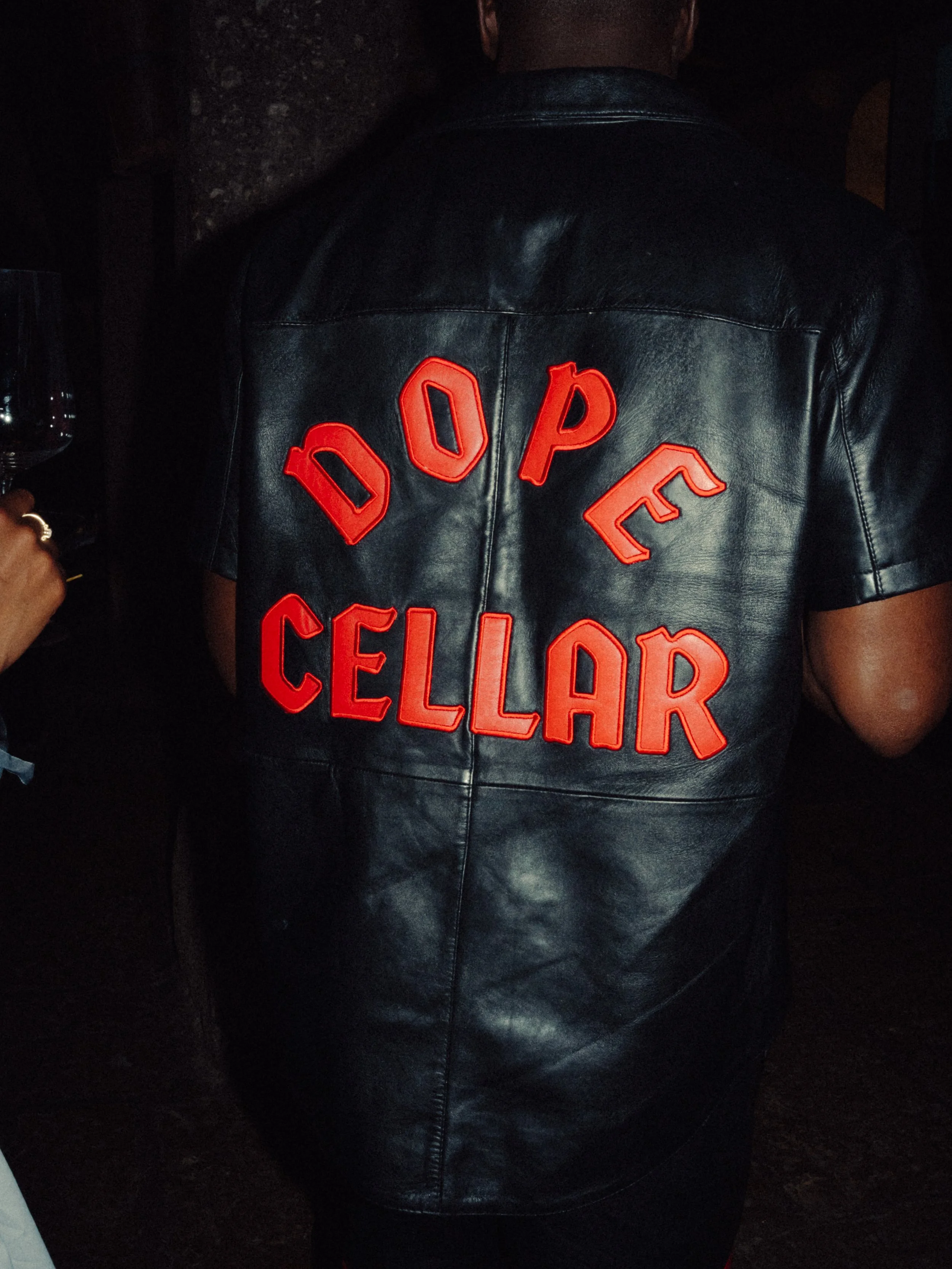 Veste en cuir noire avec le texte rouge 'DOPÉ CELLAR' écrit en lettres majuscules à l'arrière.