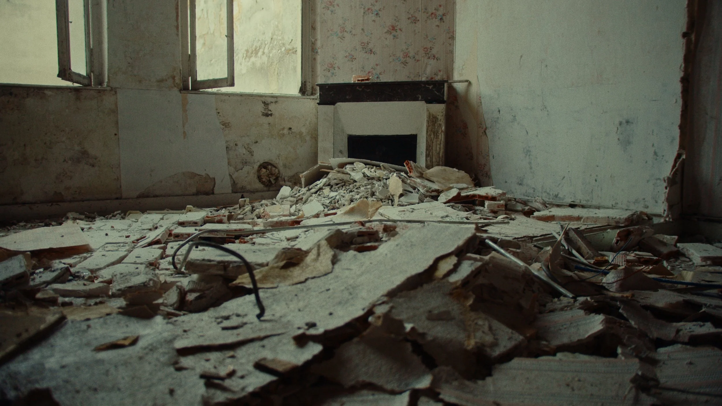 Pièce en ruine avec débris, murs abîmés, une cheminée, et fenêtre cassée laissant entrer la lumière