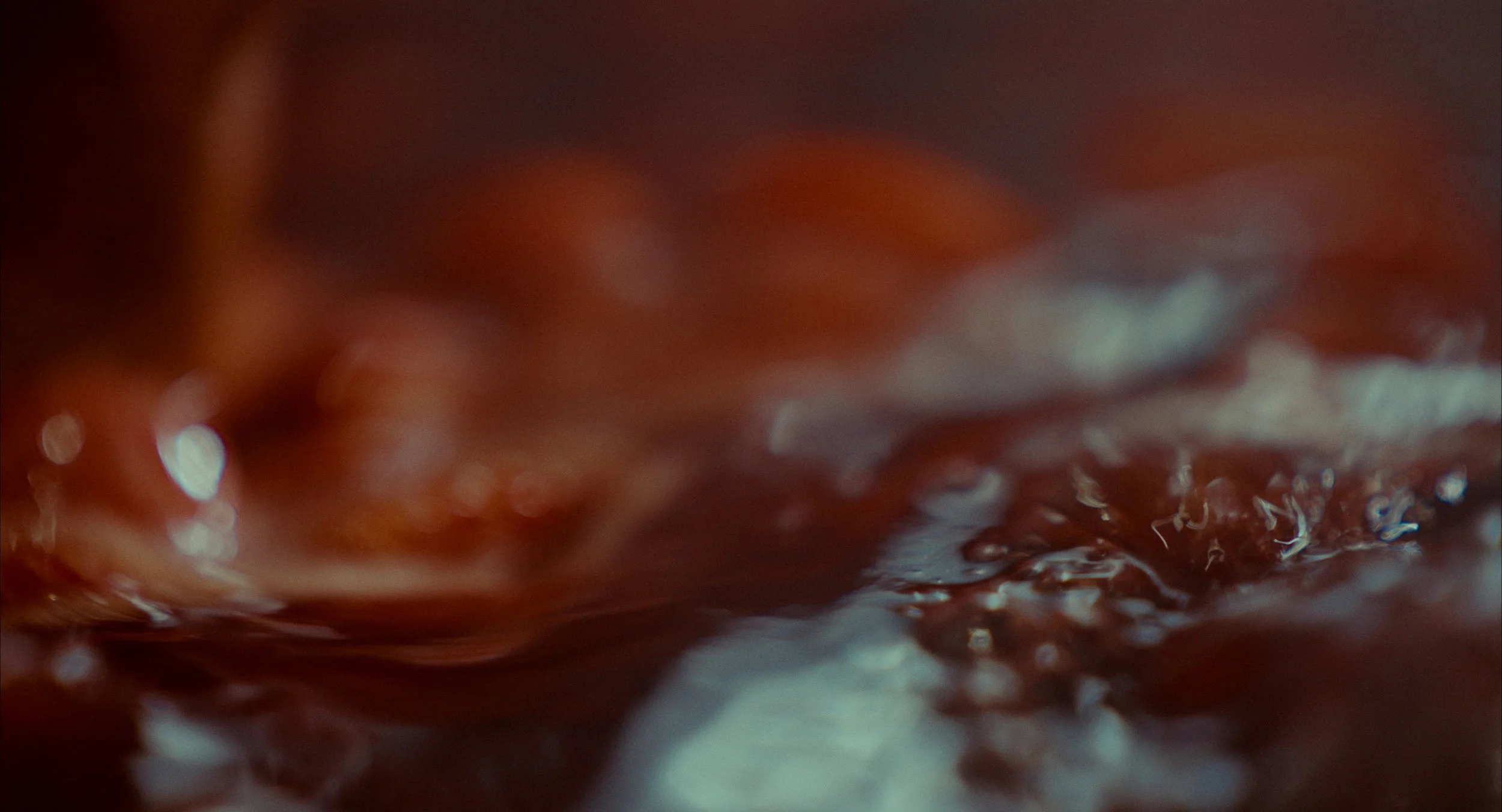 Gouttes d'un liquide brun foncé, peut-être de la sauce ou du café, très floues et proches de l'objectif.