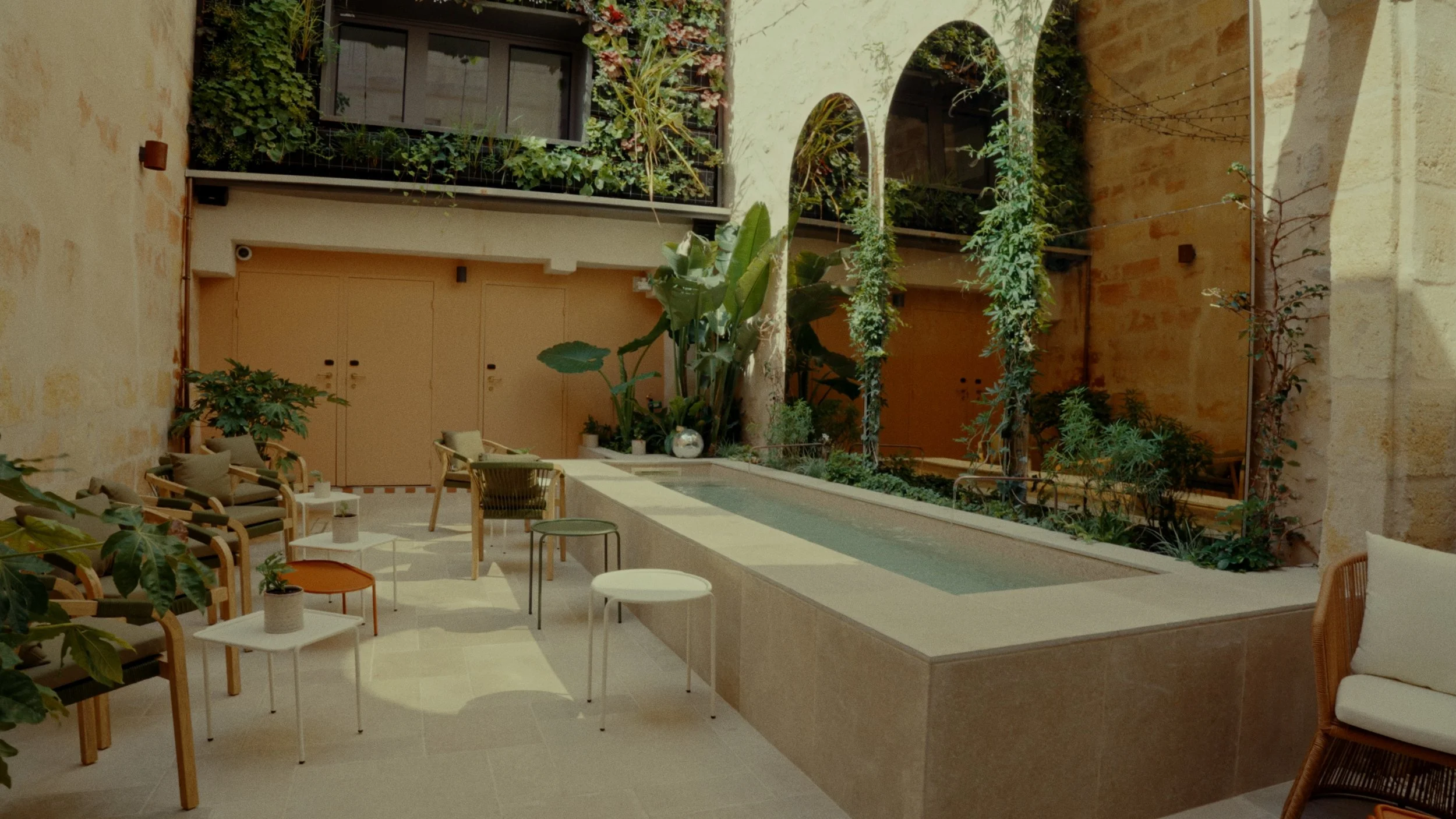 Un espace intérieur avec une fontaine centrale, des chaises et des tables, des plantes vertes et une architecture en arches.