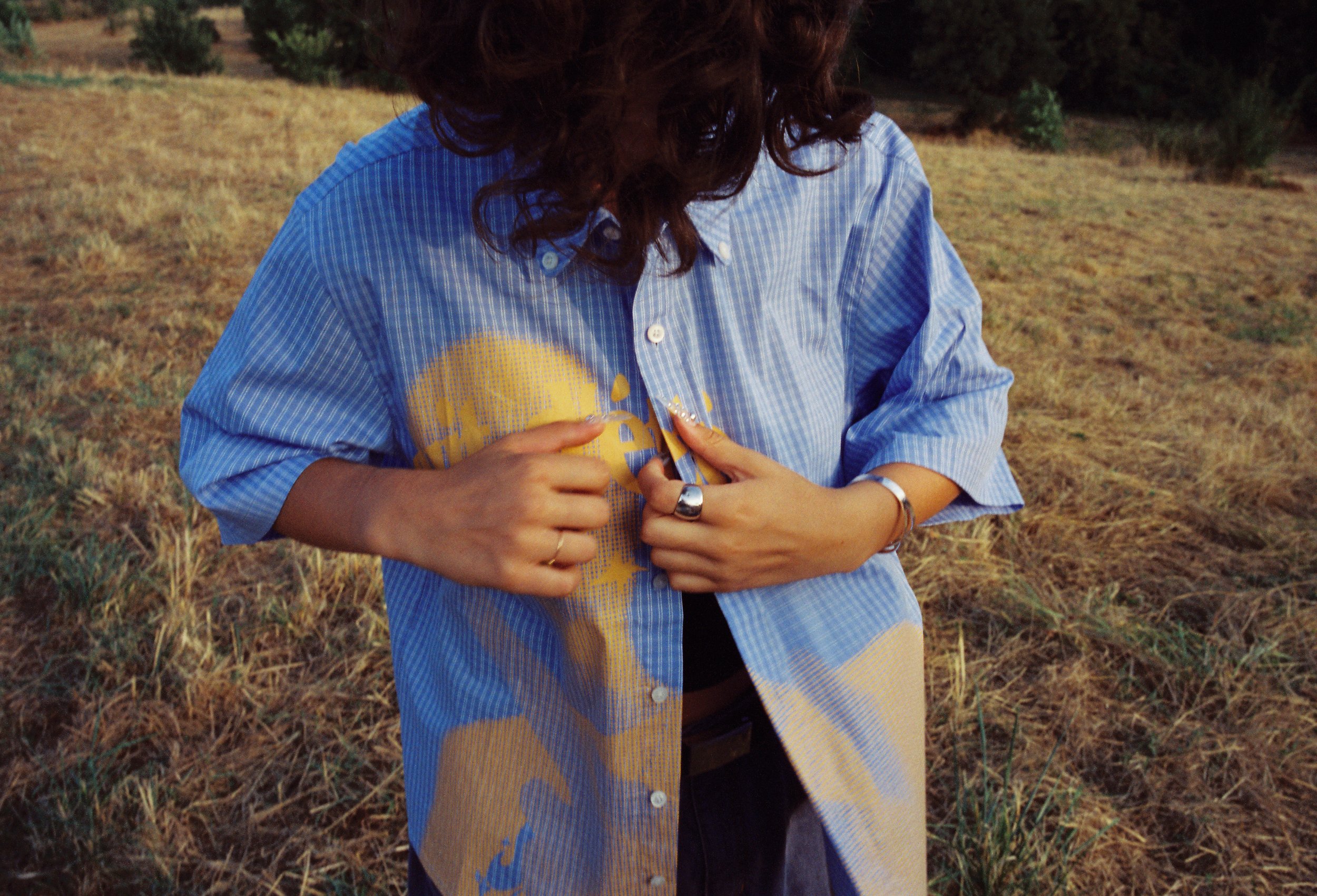 Une personne portant une chemise à carreaux bleus avec un logo jaune, dans un champ herbeux.