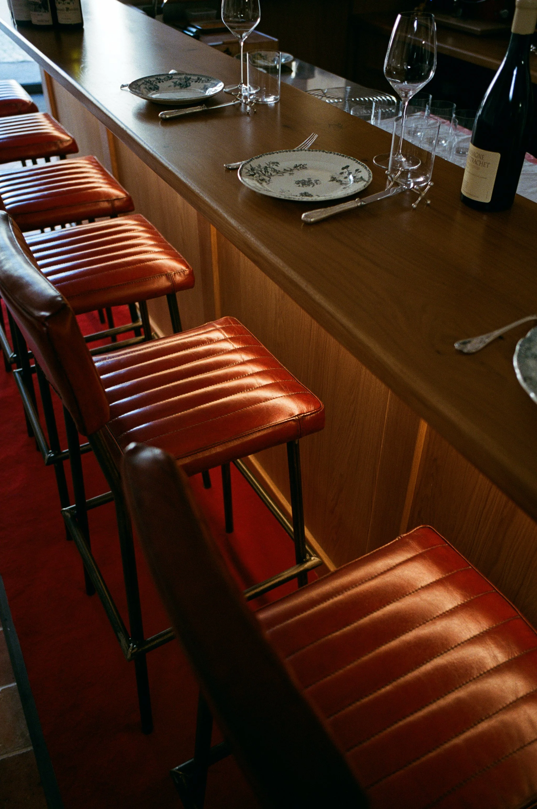 Chaise de bar en cuir marron devant un comptoir en bois avec des verres à vin, des assiettes, des fourchettes et une bouteille de champagne.