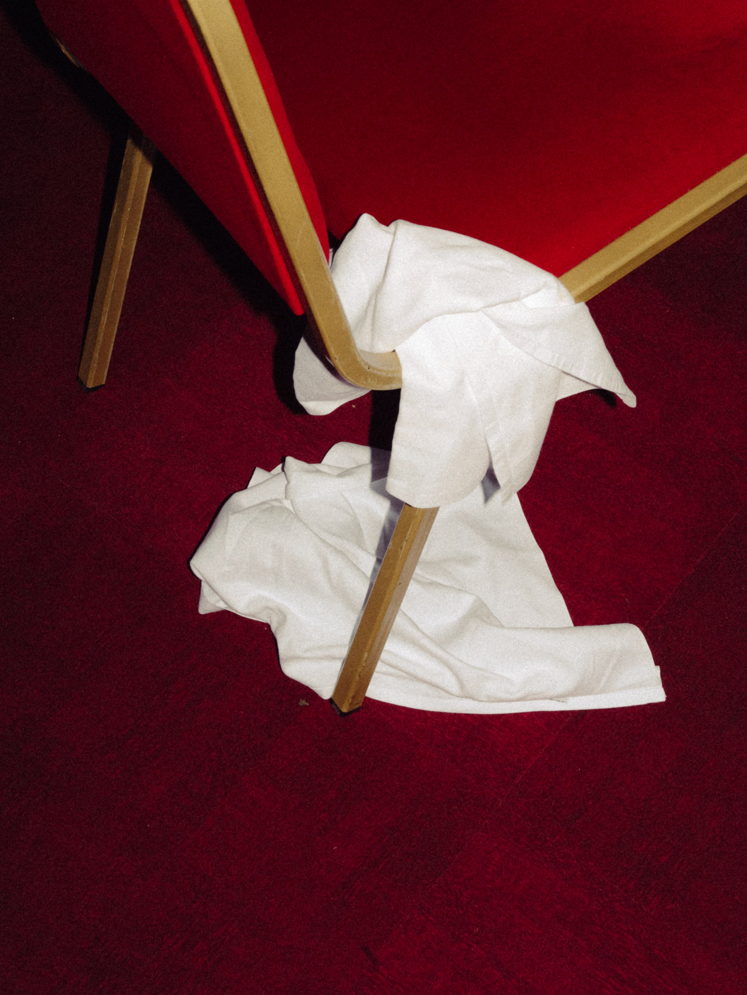 Une chaise pliable renversée avec un drap blanc qui tombe par terre, sur un tapis rouge.