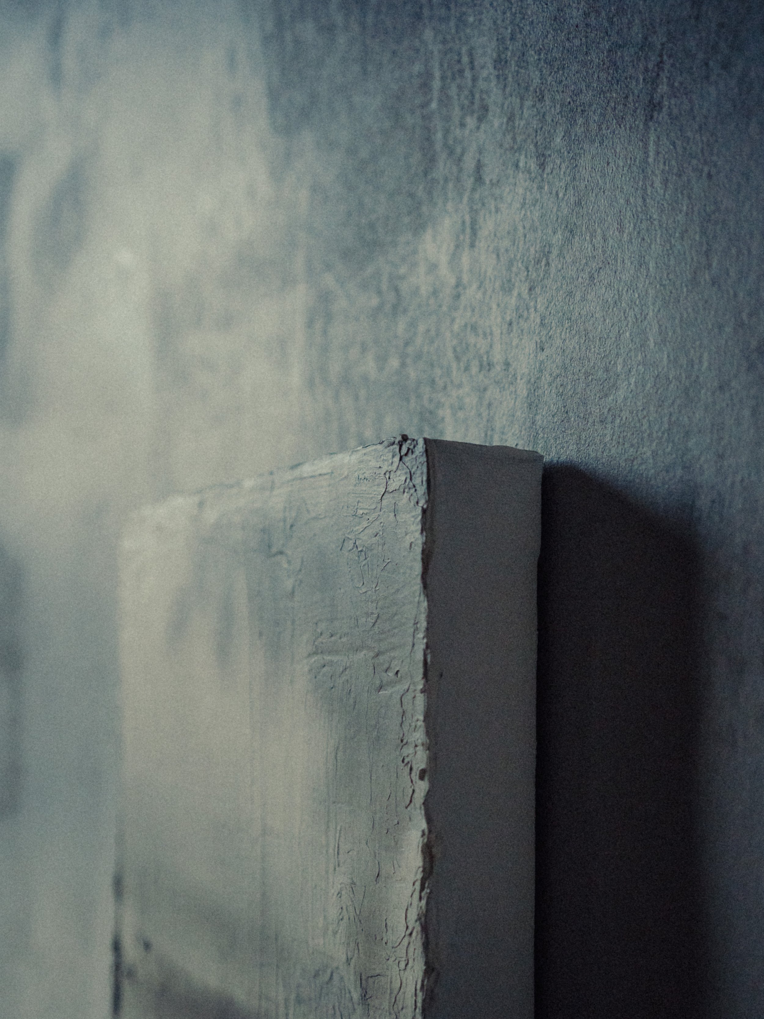 Prise de vue de côté d'un mur en plâtre craquelé et d'une poutre en bois, avec un éclairage tamisé.