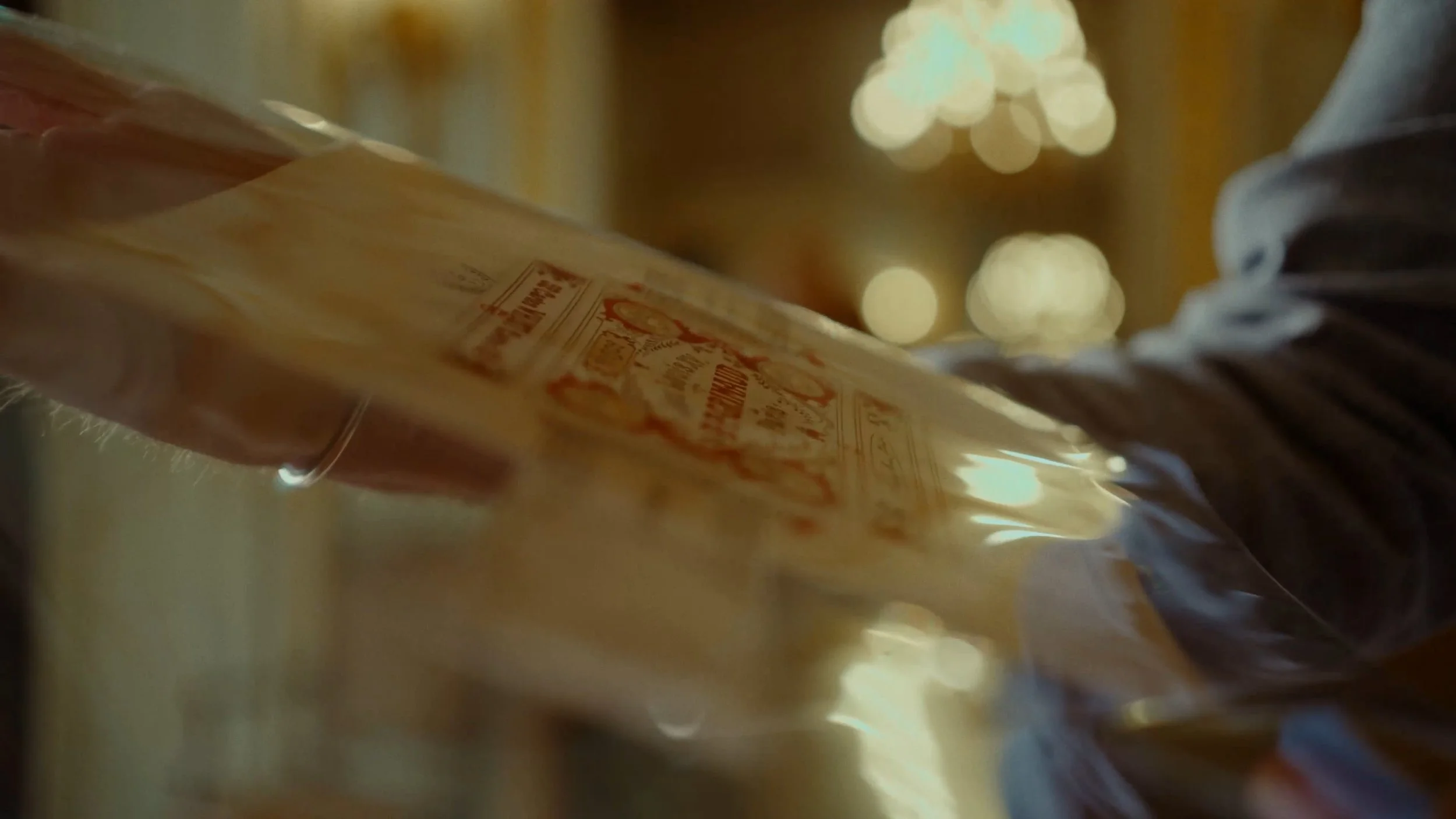 Une main tenant un sac en plastique contenant un produit avec une étiquette rouge, dans un environnement éclairé avec des lumières floues en arrière-plan.