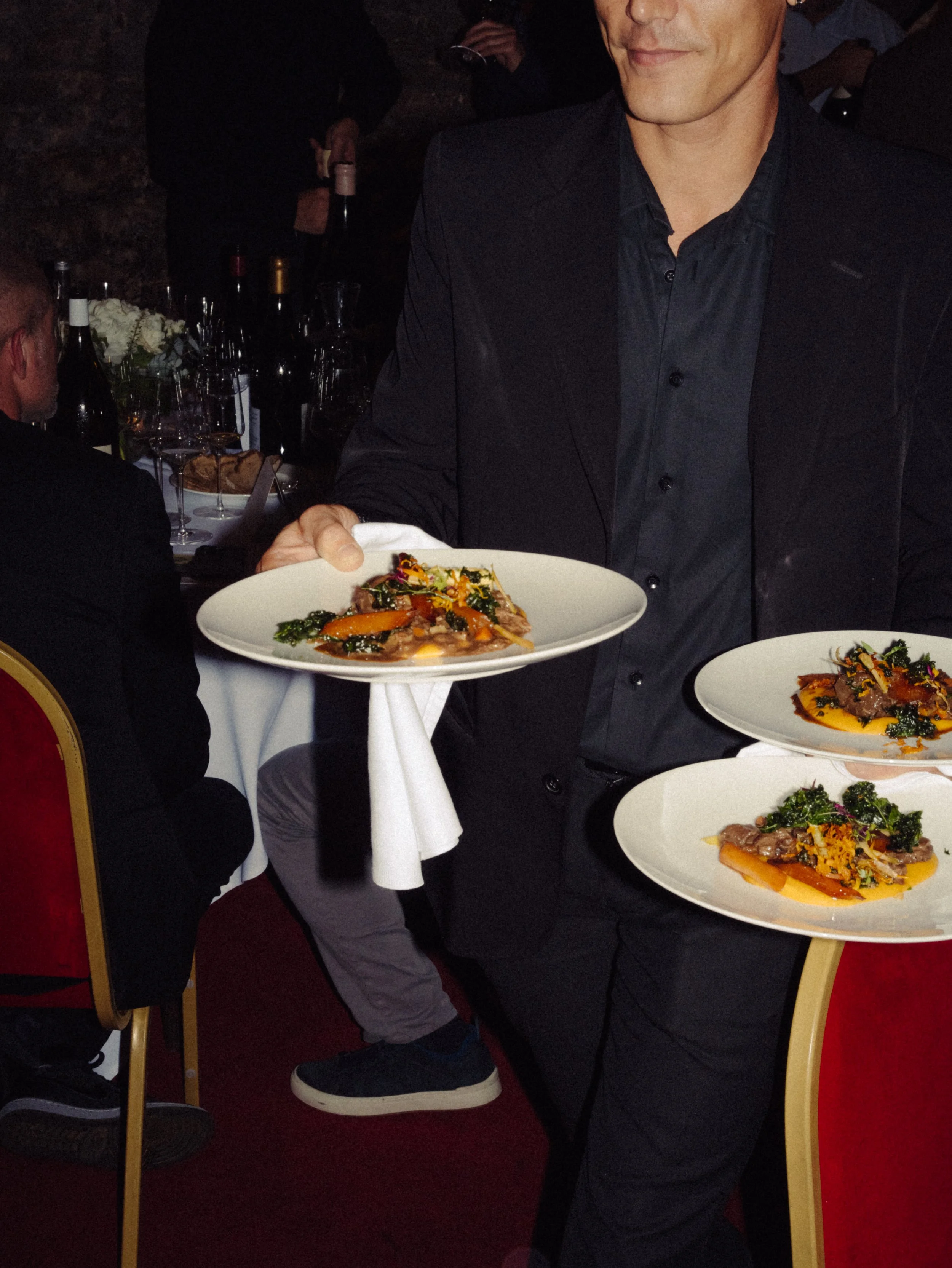 Homme portant un costume noir servant des assiettes de nourriture dans un restaurant élégant.