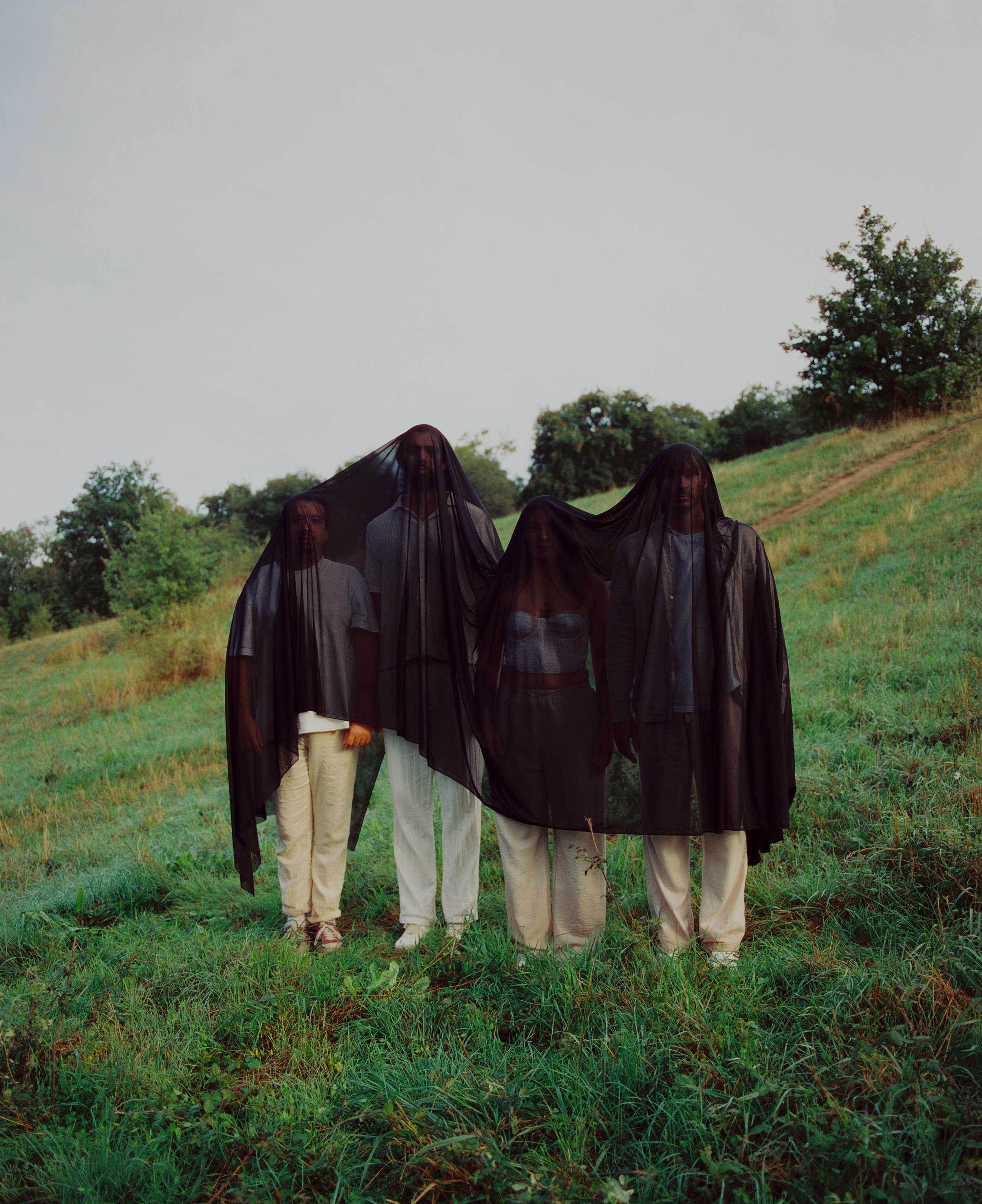 Quatre personnes debout dans un champ vert, deux portant des voiles noirs sur la tête, photographiées lors d'une journée nuageuse.