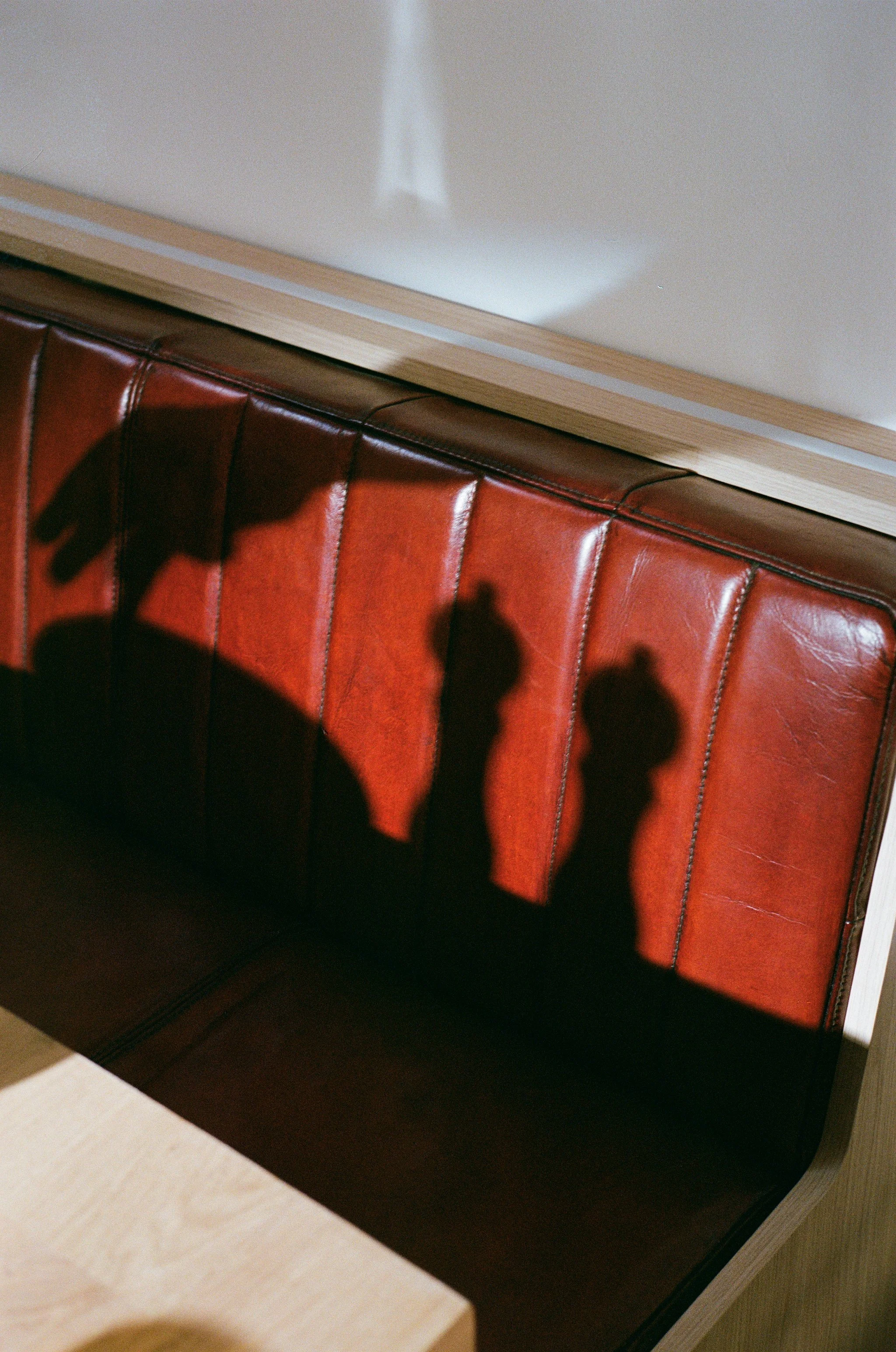 Ombres de trois bouteilles de parfum projetées sur une banquette en cuir rouge.