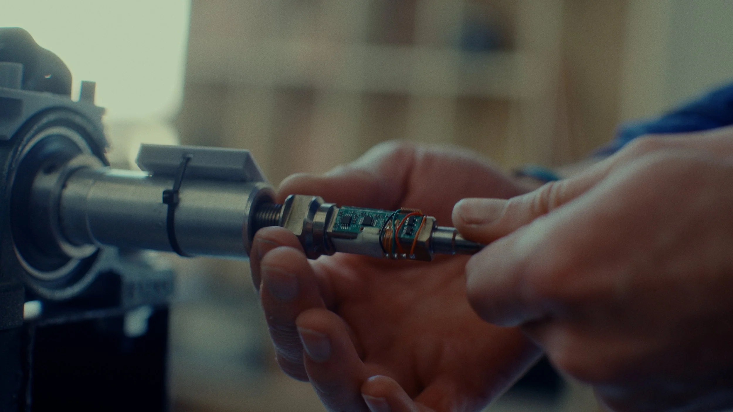 Une personne manipule un composant électronique fixé à un arbre mécanique, probablement dans un laboratoire ou un atelier de haute technologie.