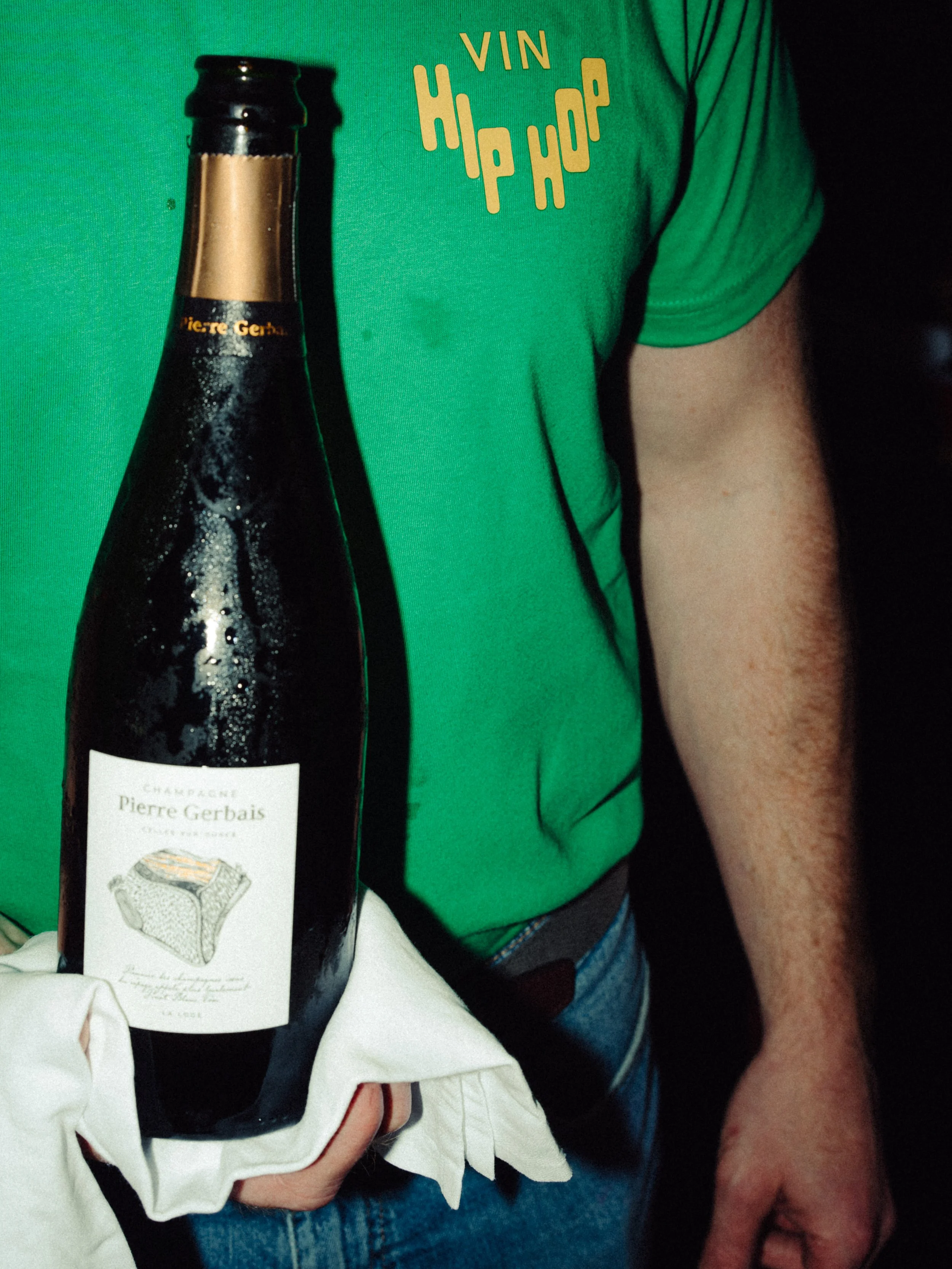 Person tenant une bouteille de champagne Pierre Gervais, portant un t-shirt vert avec le texte 'Vin Hip Hop'.