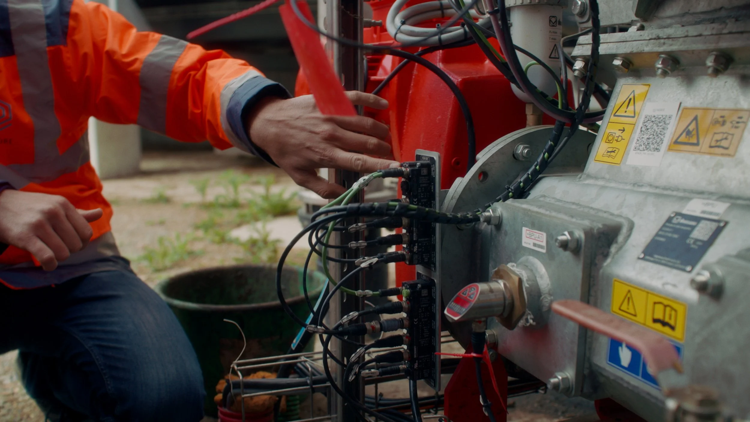 Un technicien effectue des réparations sur une machine industrielle complexe avec des câbles et des composants métalliques.