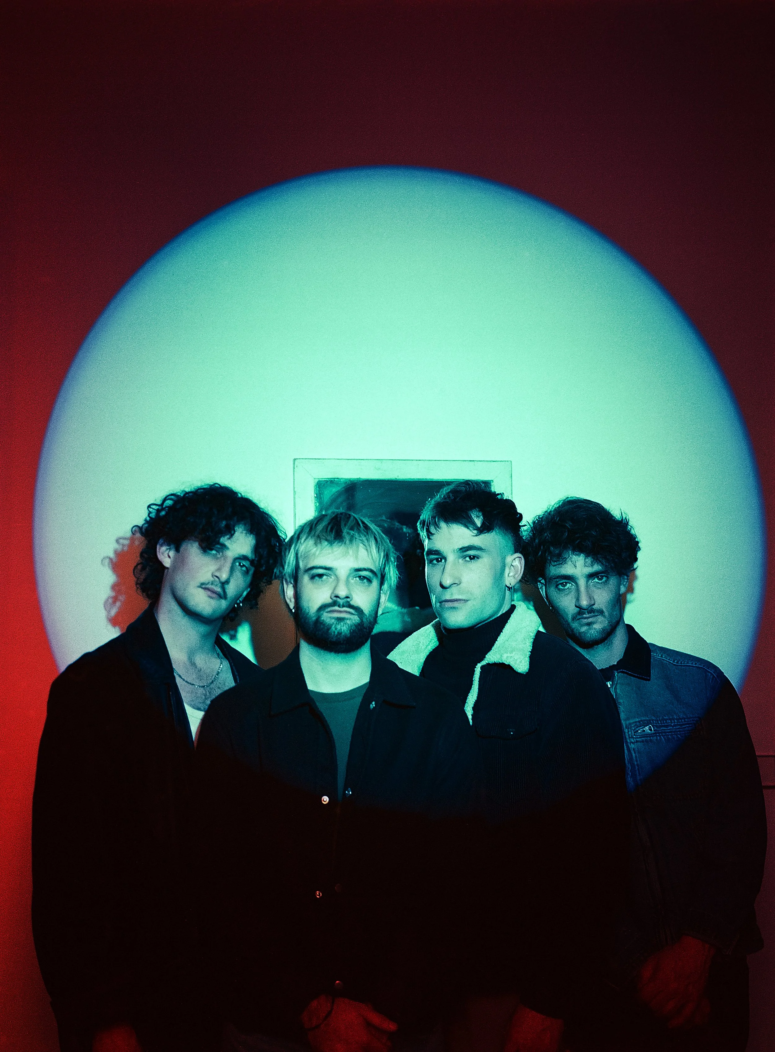 Un groupe de quatre jeunes hommes posant devant une lumière colorée, avec un miroir derrière eux.