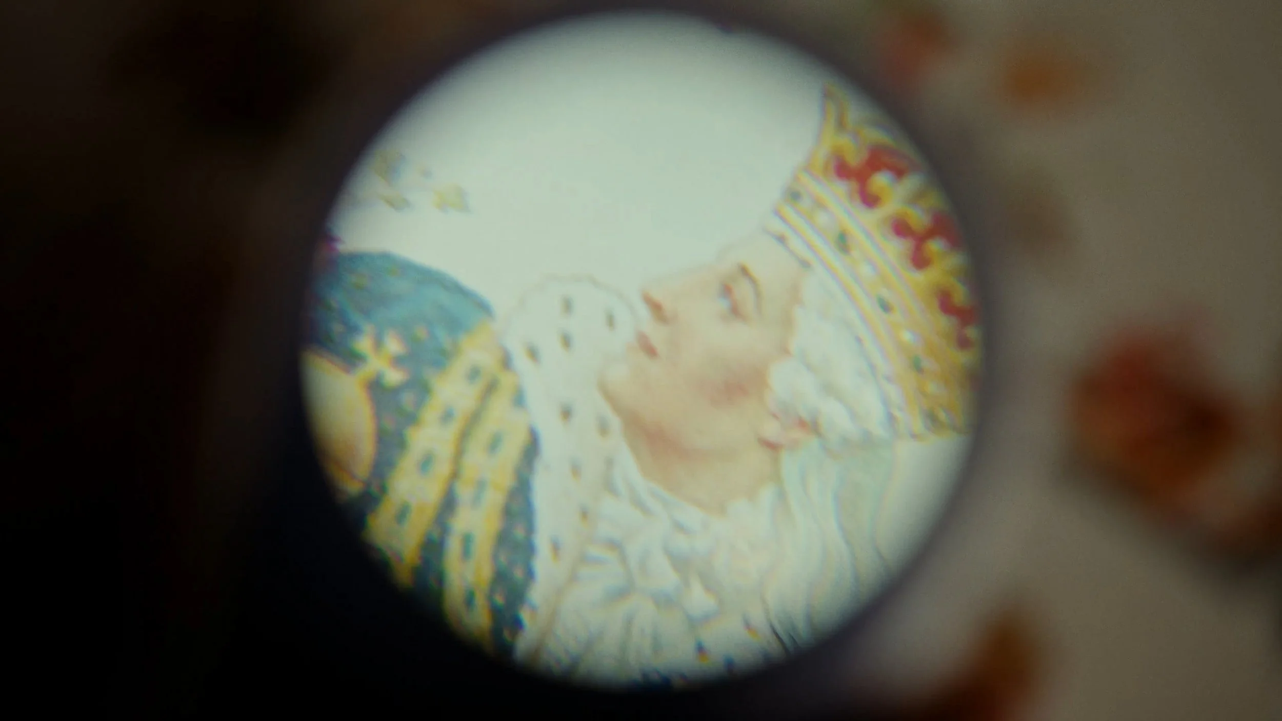 Une image vue à travers une loupe représentant une jeune fille portant une couronne, avec des cheveux blonds et un vêtement blanc, dans un décor coloré.