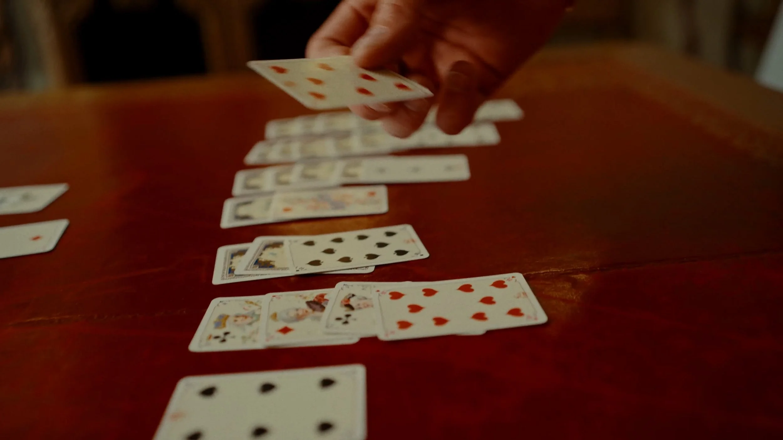 Mains manipulant un jeu de cartes sur une table en bois rouge foncé.