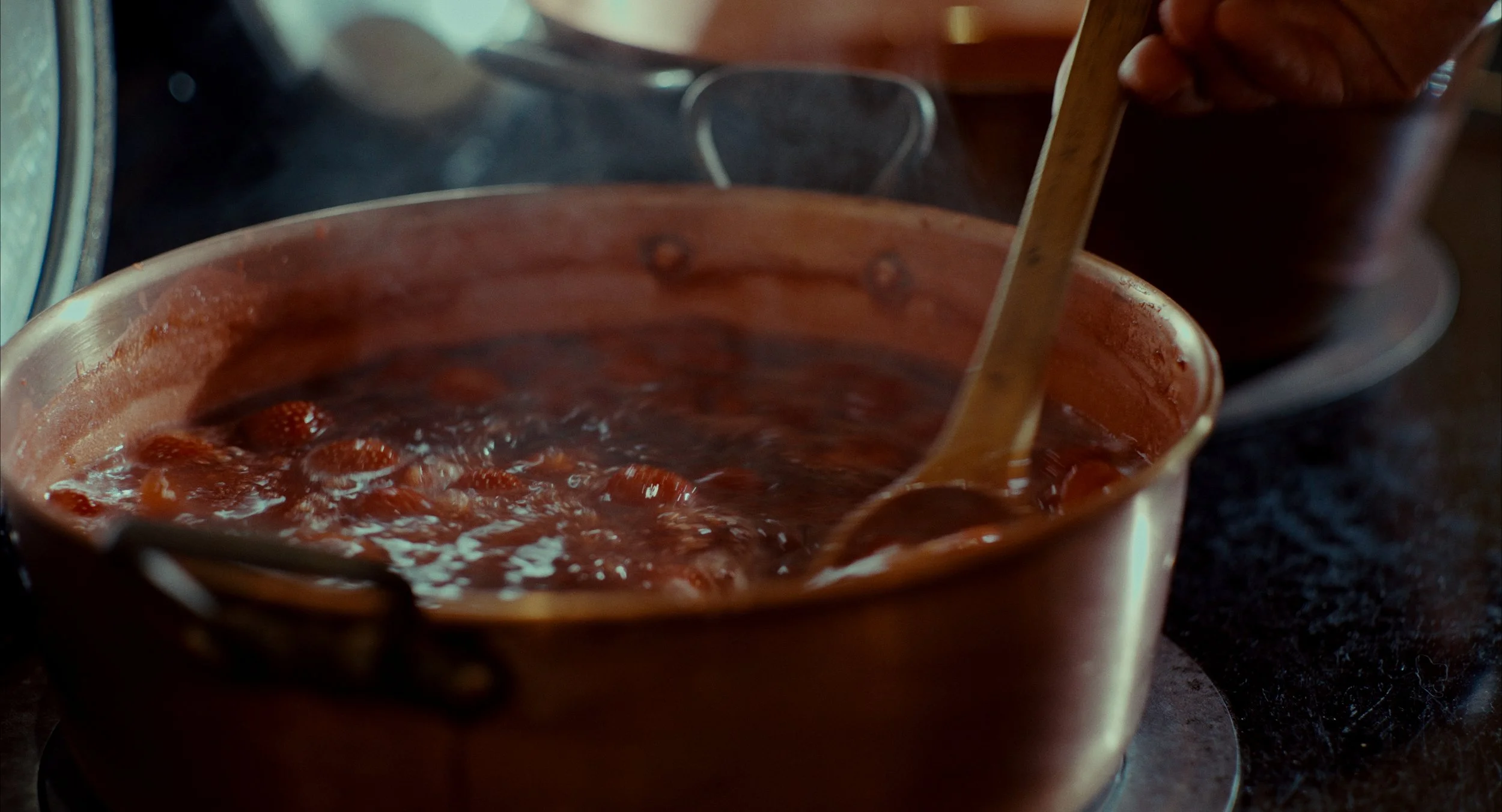 Une casserole contenant une sauce ou une confiture en train de mijoter, avec une cuillère en bois pour remuer.