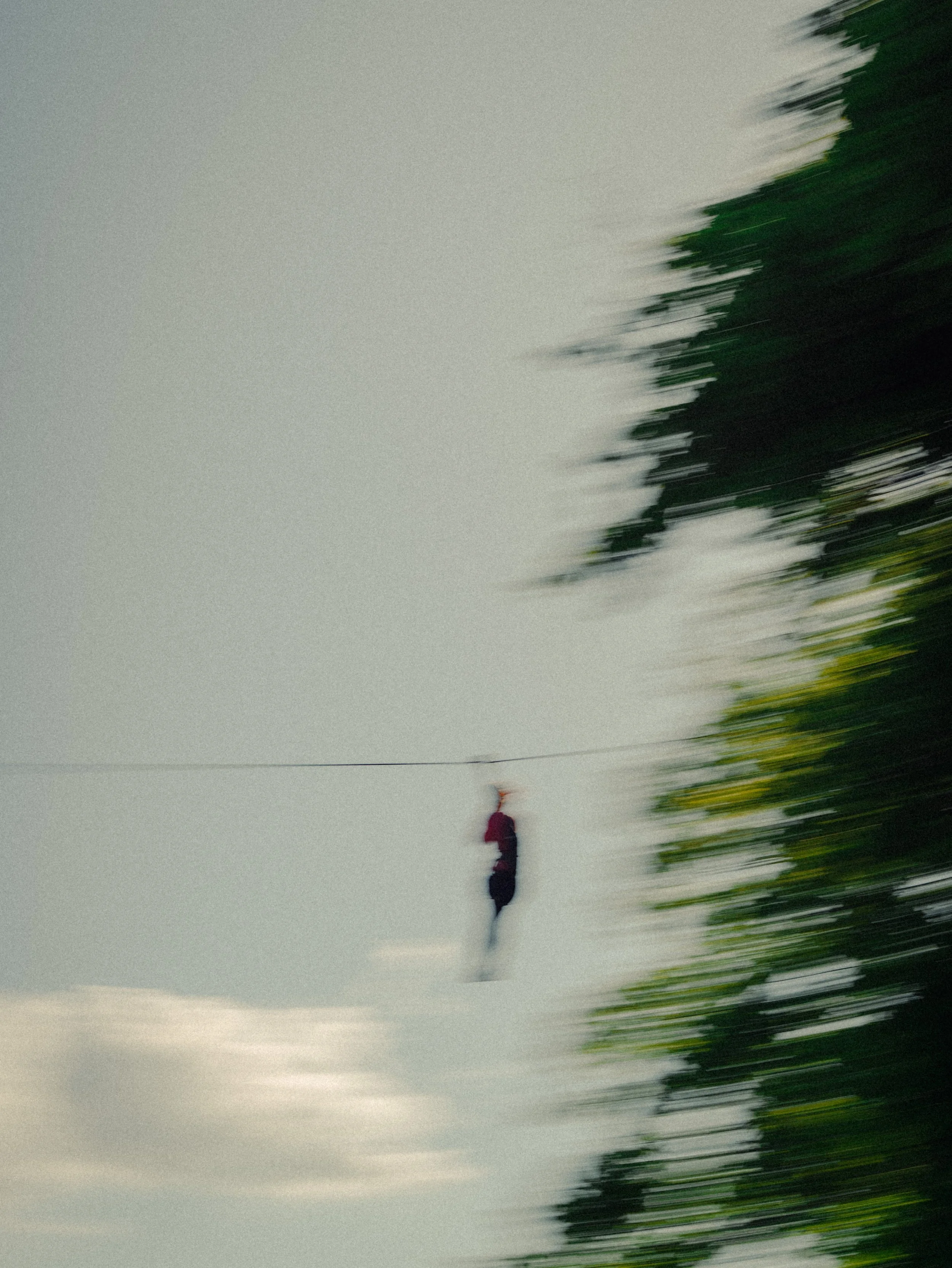 Person marchant sur une corde tendue dans le ciel, avec des arbres verts en arrière-plan et un ciel nuageux.