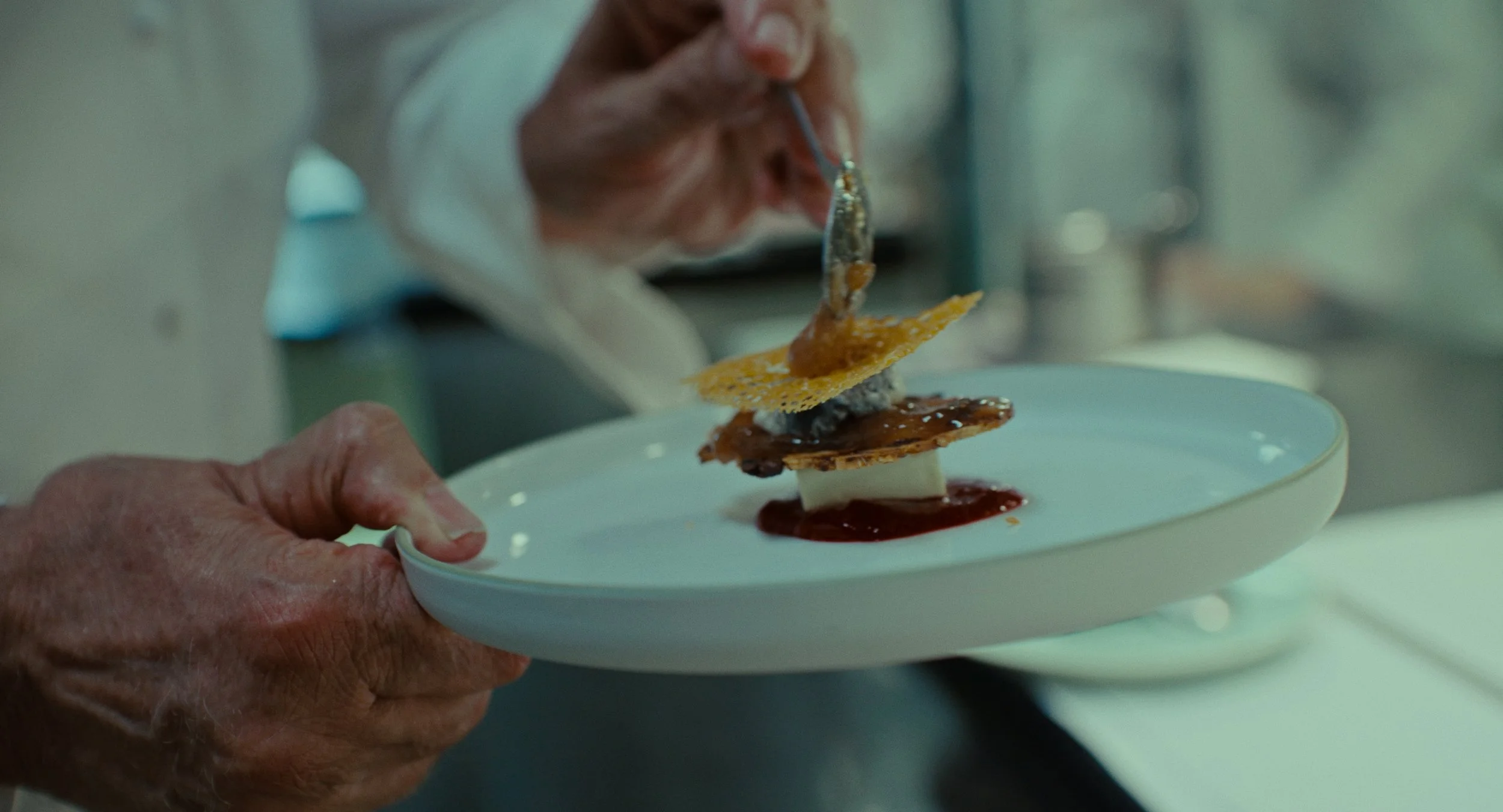 Chef dépose un plat de cuisine sophistiquée avec plusieurs couches et textures différentes dans une assiette blanche.