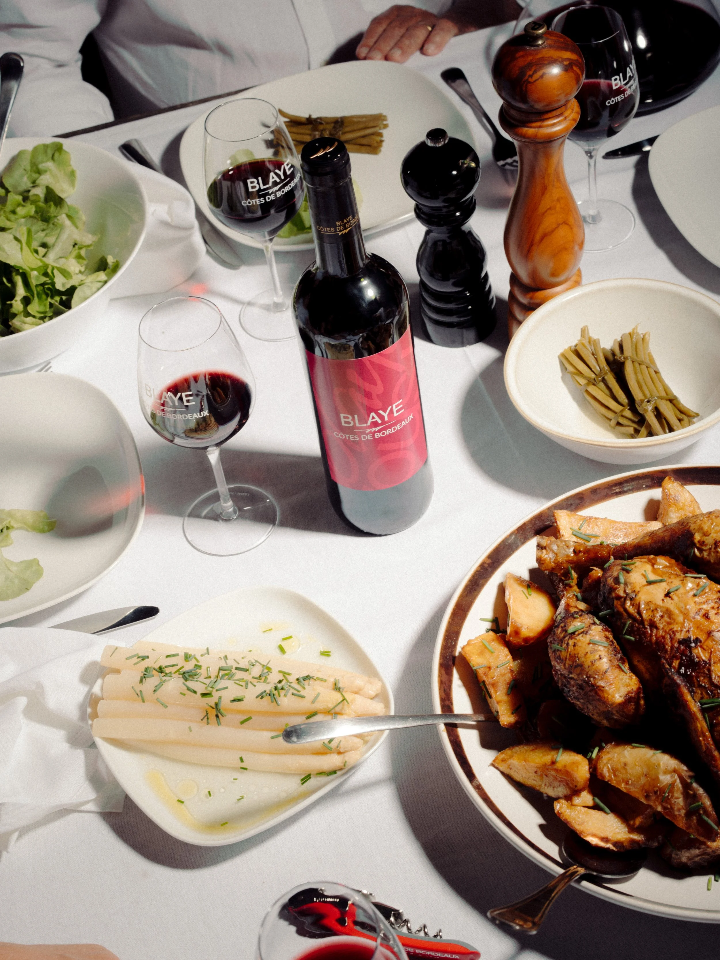 Une table dressée avec du vin, une salade, des pâtes, un plat de viande, du fromage, et des condiments.