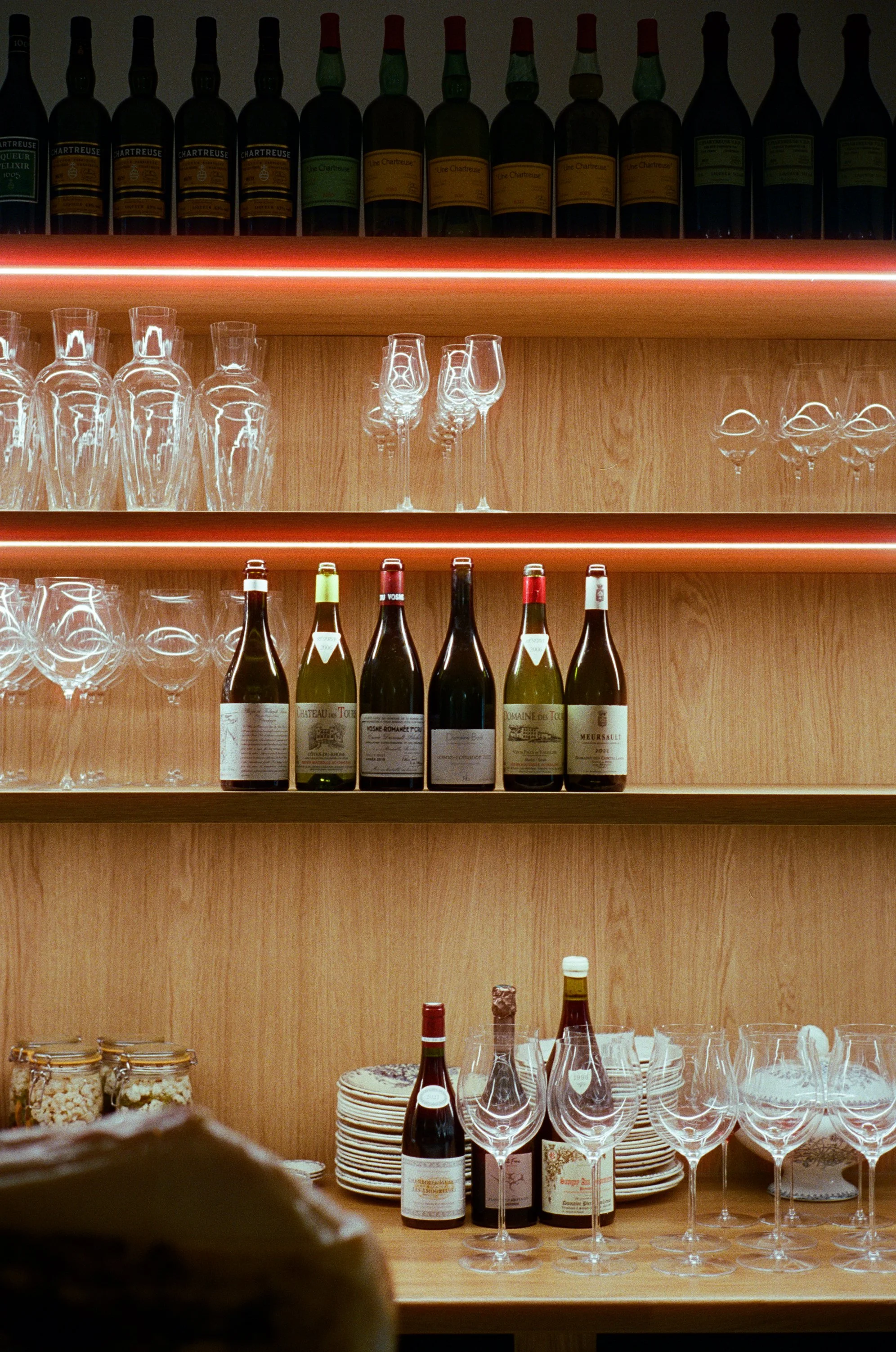 Étagères en bois avec des bouteilles de vin, des verres à vin et des plateaux en verre pour la dégustation.