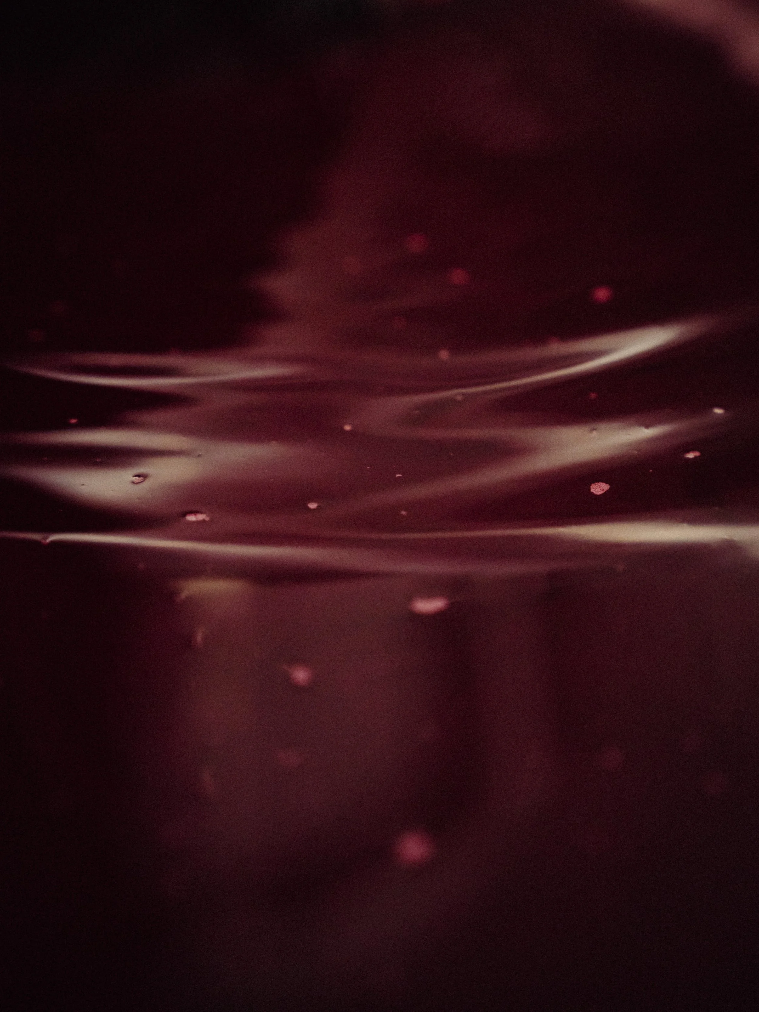 Surface lisse d'une substance sombre avec des reflets roses et des petites bulles ou particules flottant.