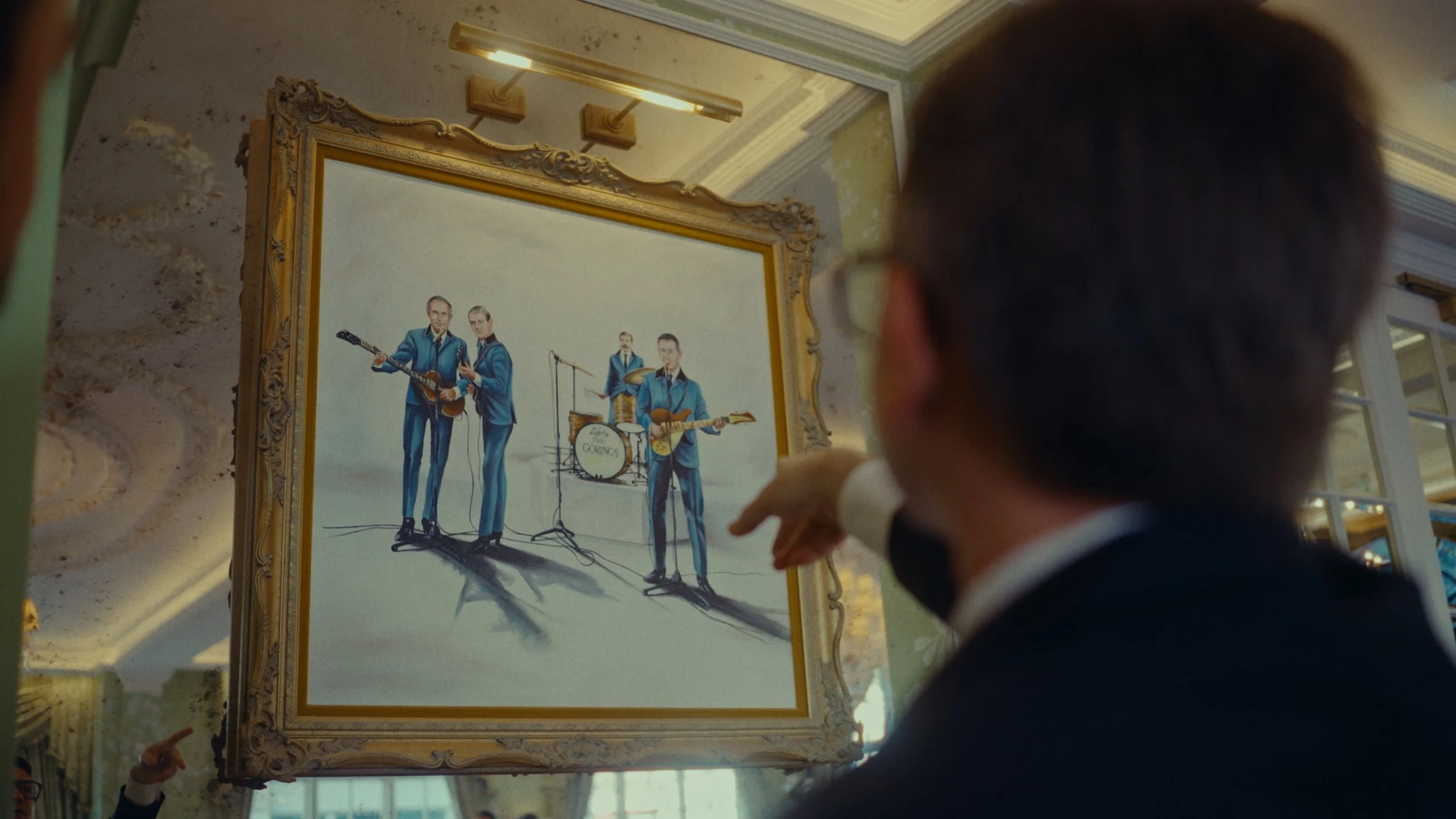 Un homme en costume noir et chemise blanche regarde un tableau de style caricature représentant un groupe de musiciens en costumes bleus jouant de la musique.
