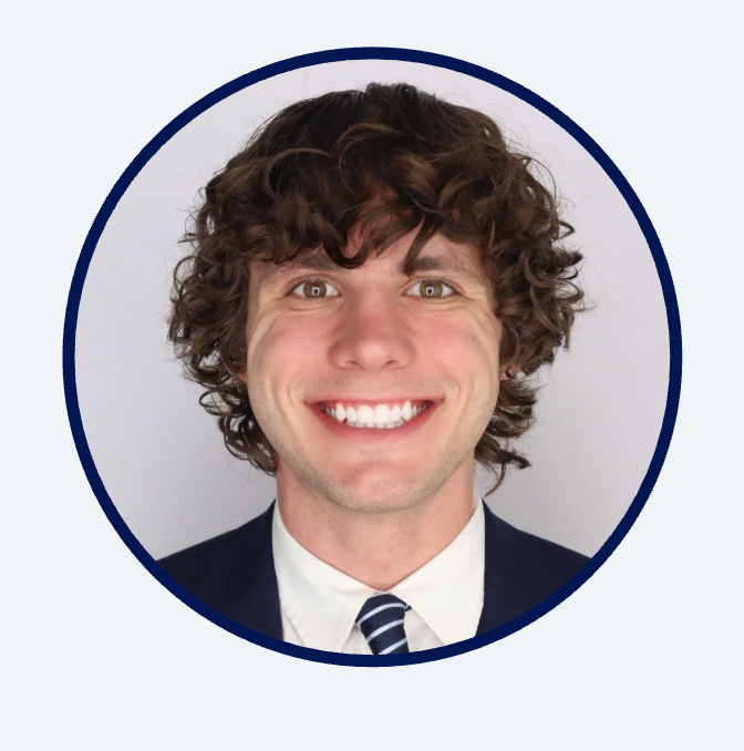 Smiling man with curly brown hair wearing a suit and tie.