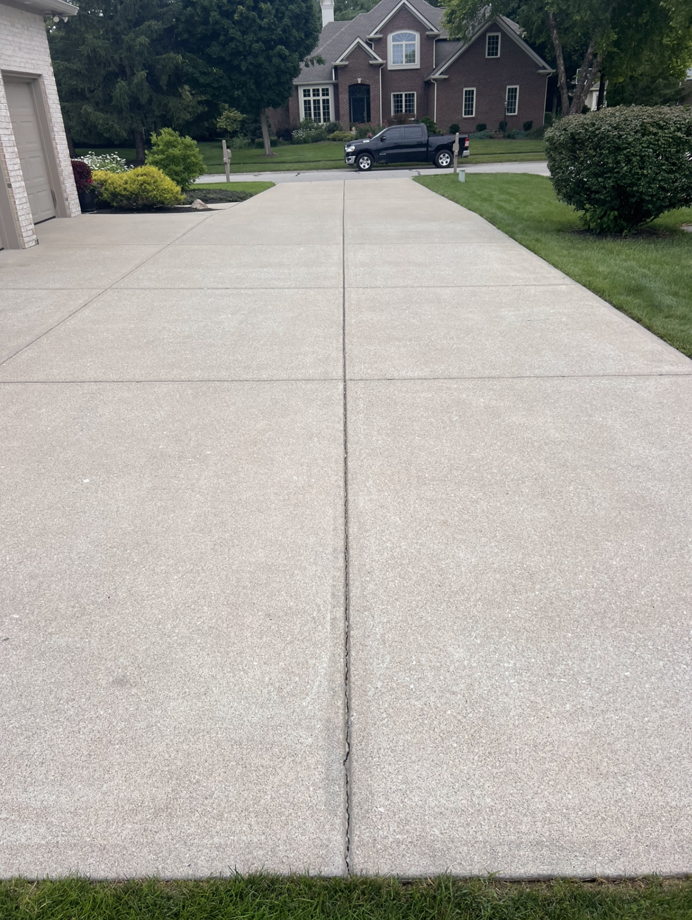 Freshly poured concrete driveway in front of a suburban house with green grass and trees.