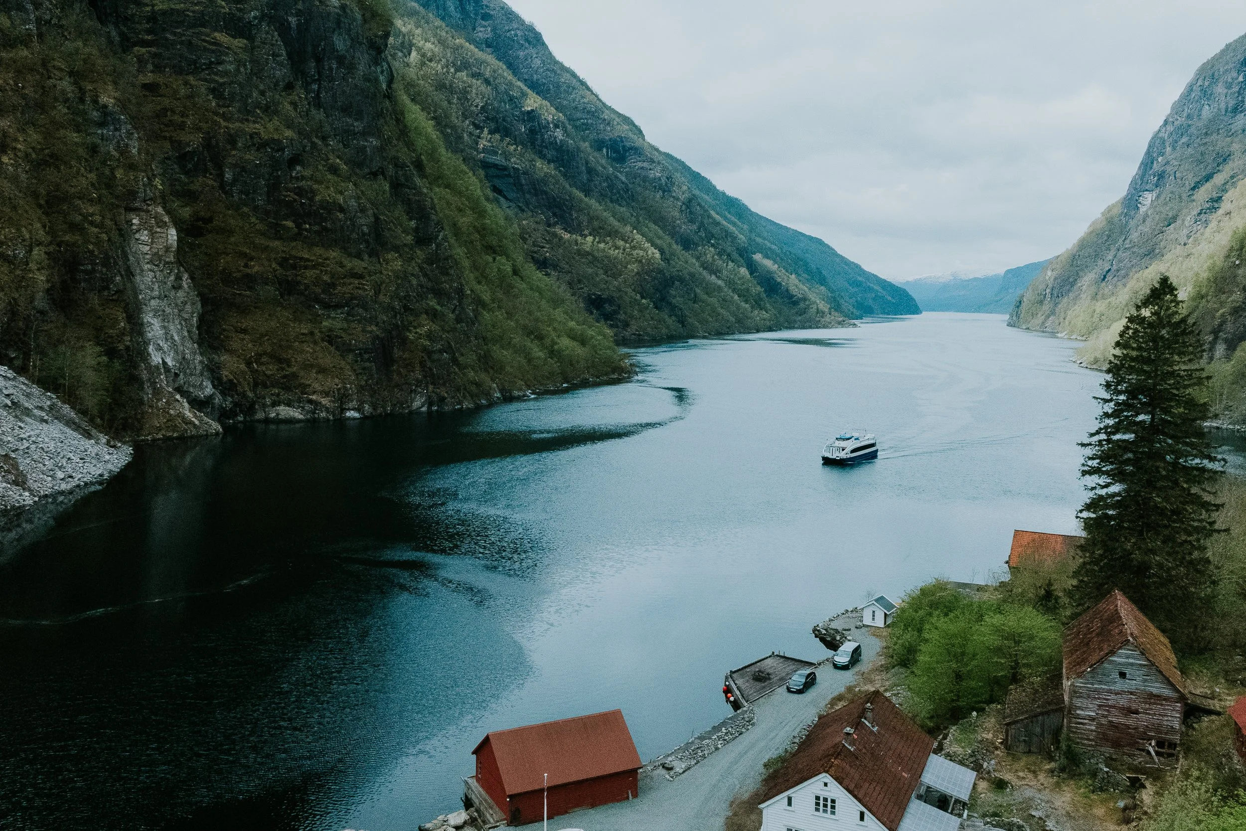 Fjord med fjell på begge sider, og en båt som kjører i vannet. Liten landsby med hus nederst i bildet.