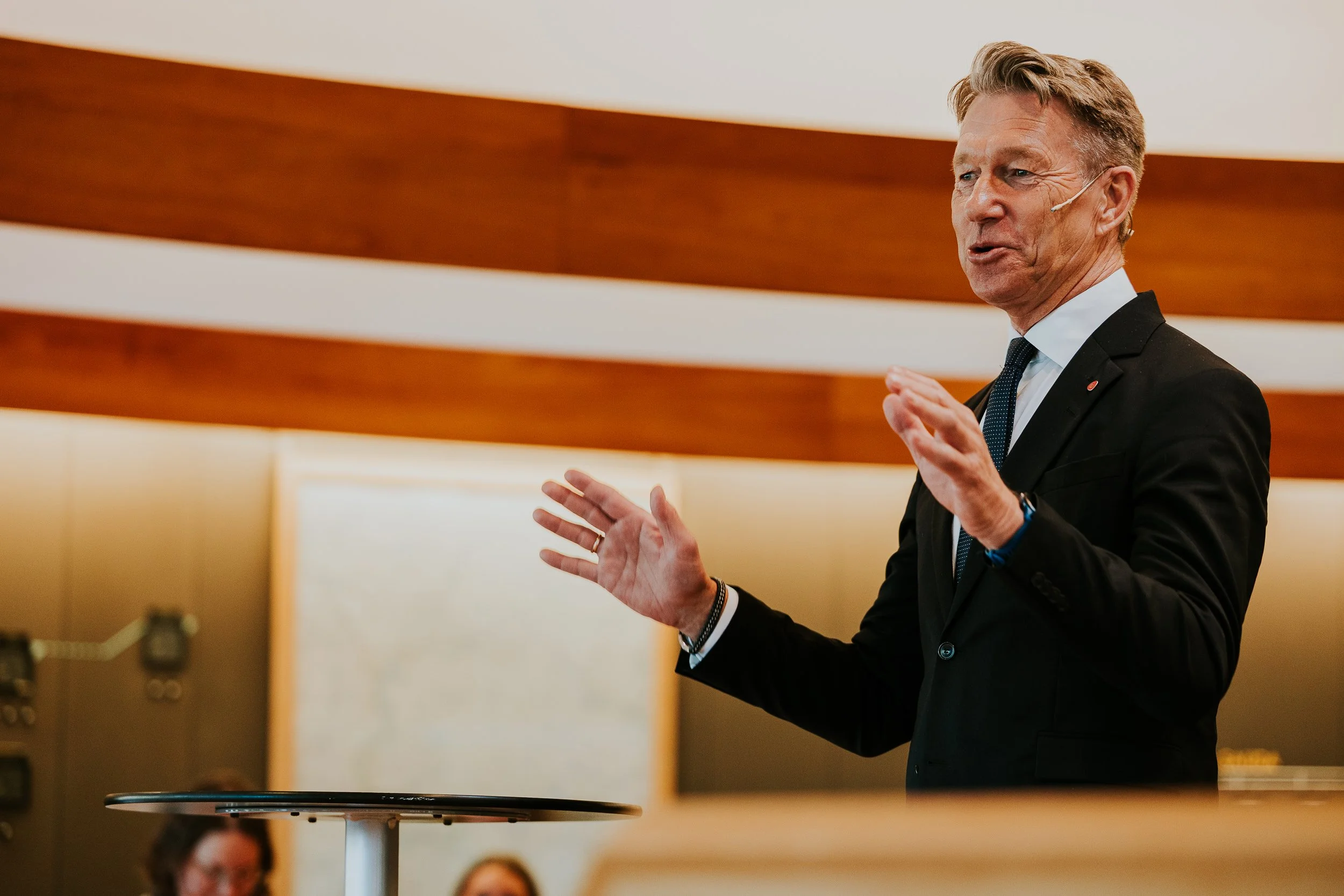 En mann i dress som holder en tale eller presentasjon i et møterom eller konferansesal.